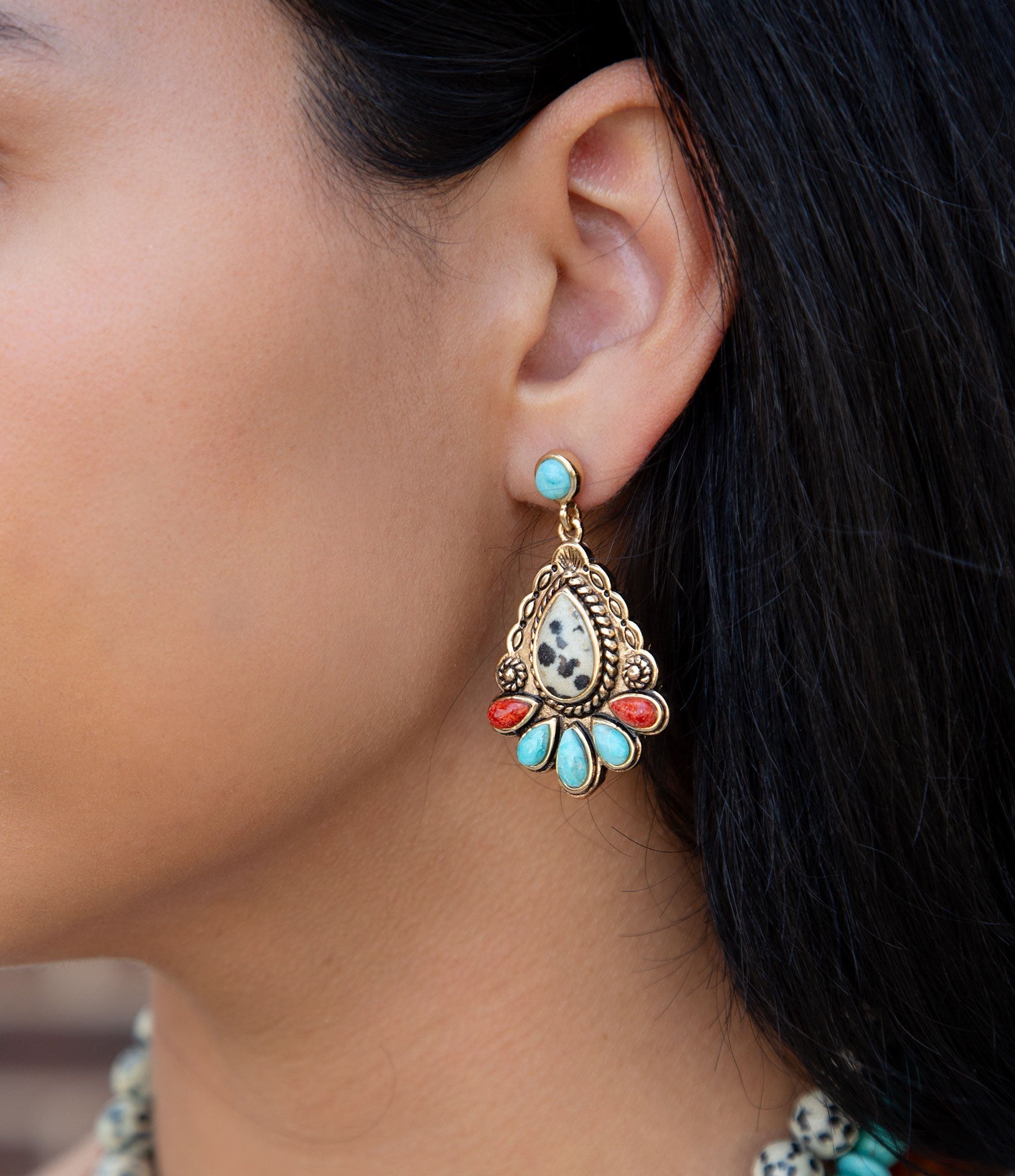 Close-up of an ear wearing a decorative earring with turquoise and red stones.