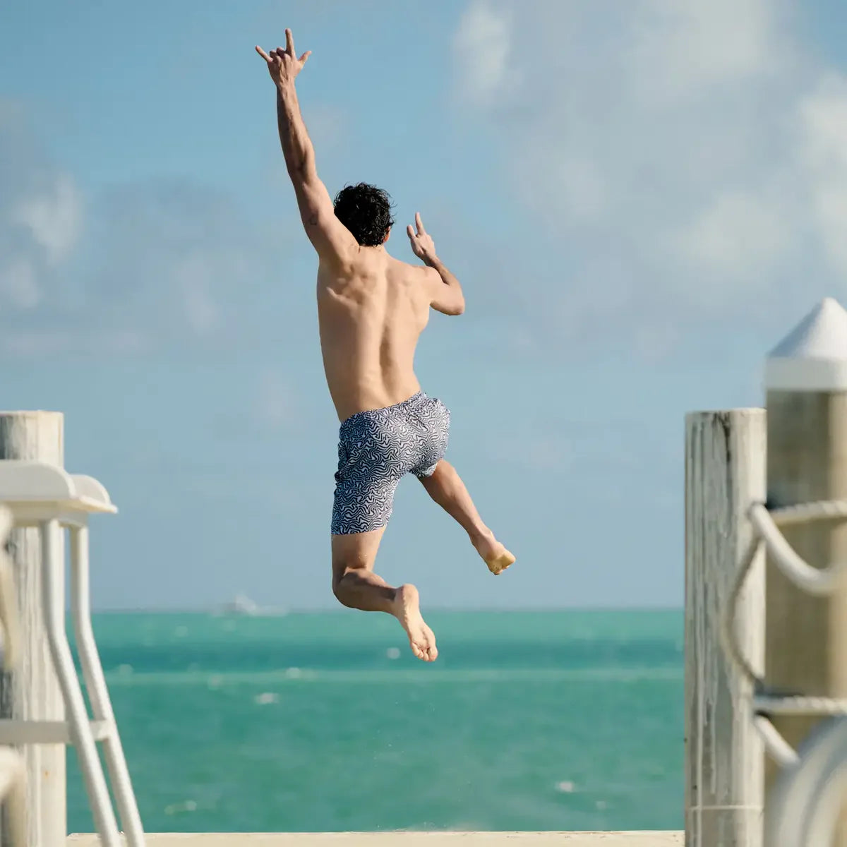Man jumping off a dock into the ocean with clear blue sky and water.