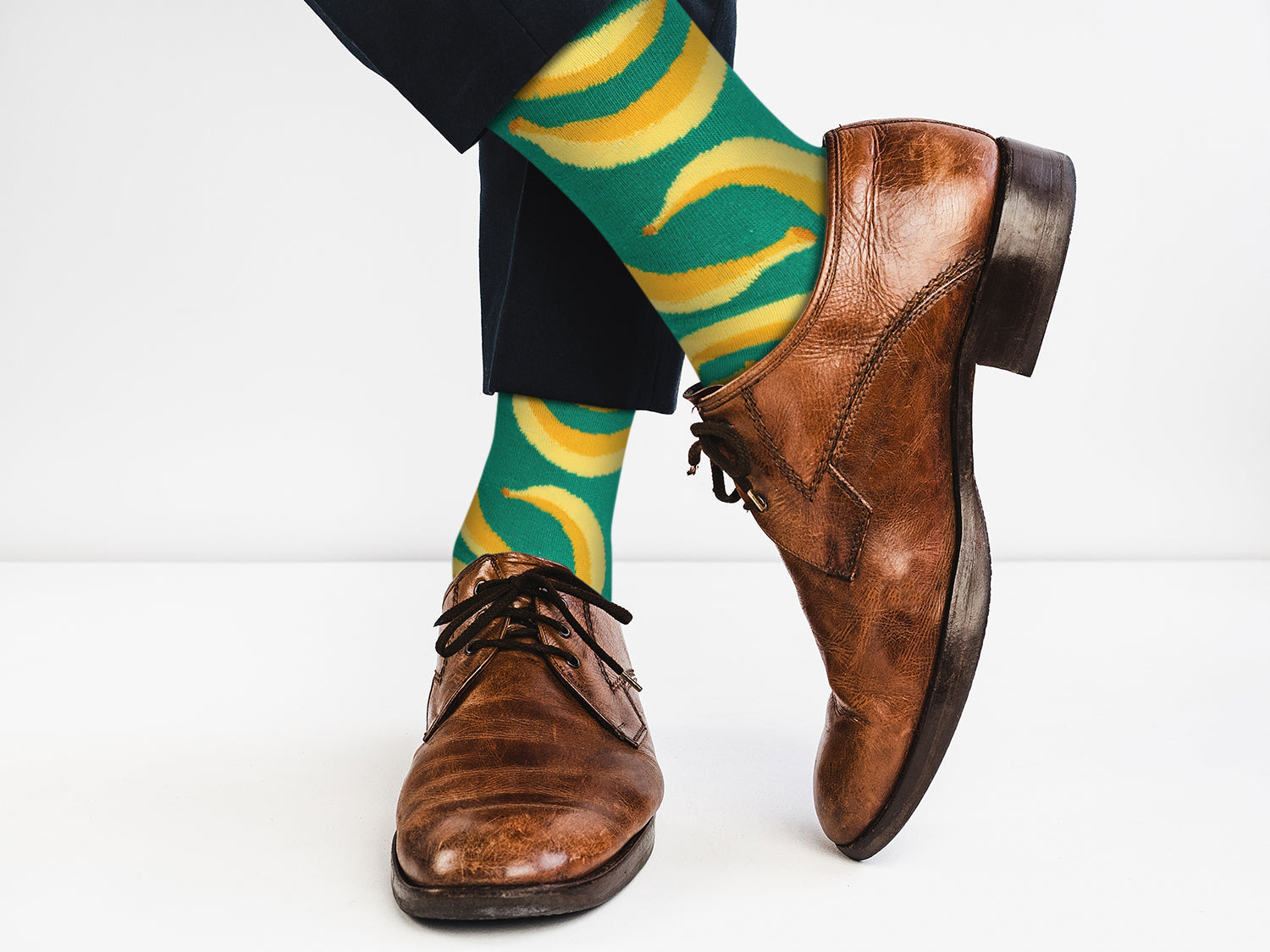 Brown dress shoes with green socks featuring banana pattern on a white background