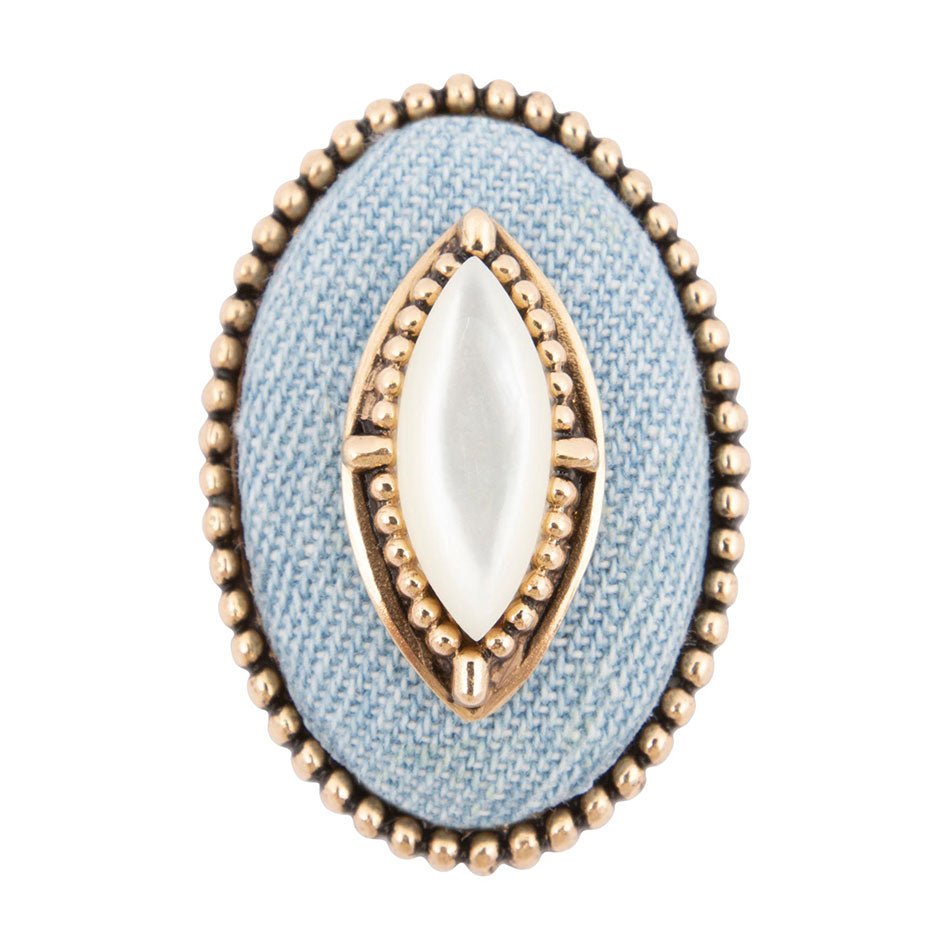 Decorative ring with gold and white stone on a light blue fabric background