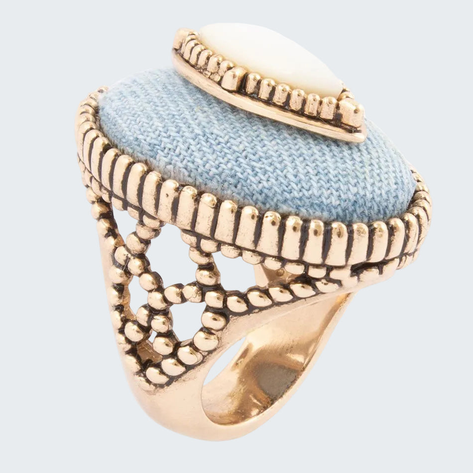 Gold ring with a textured band and light blue fabric center on a white background