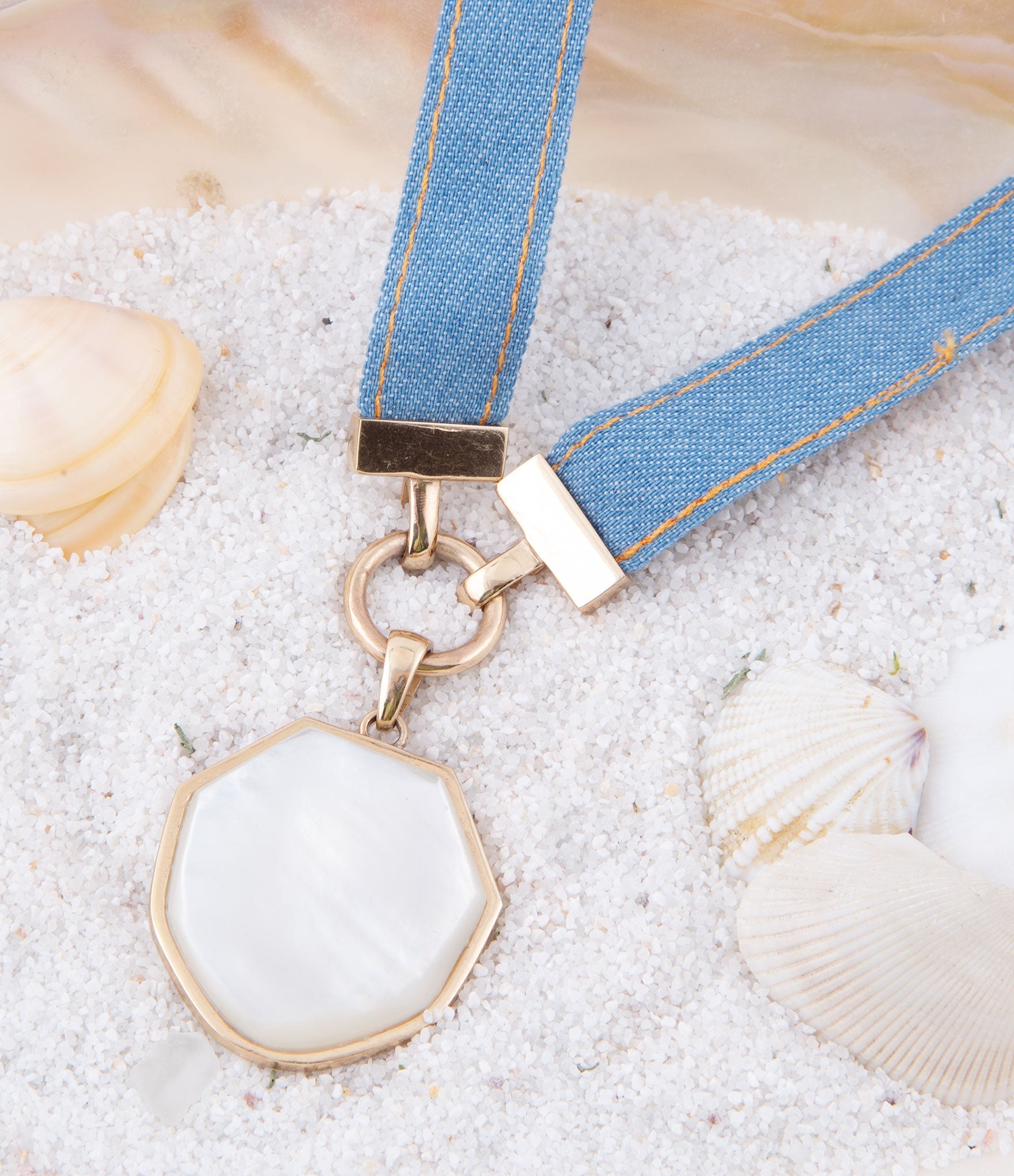 Keychain with a blue strap and white pendant on sand with shells