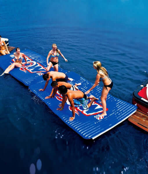 Group of people on a large inflatable water mat with logos in a body of water.