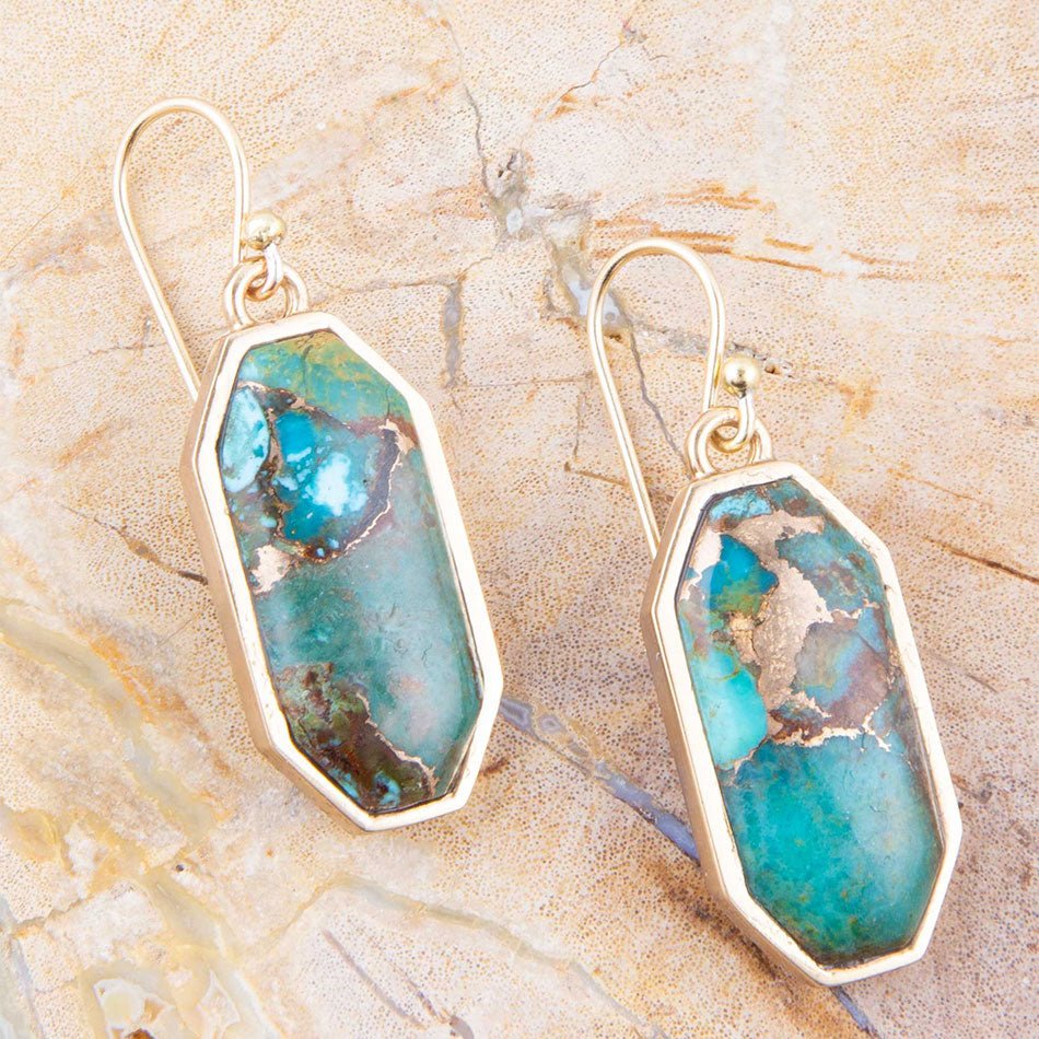 Turquoise stone earrings on a beige stone background