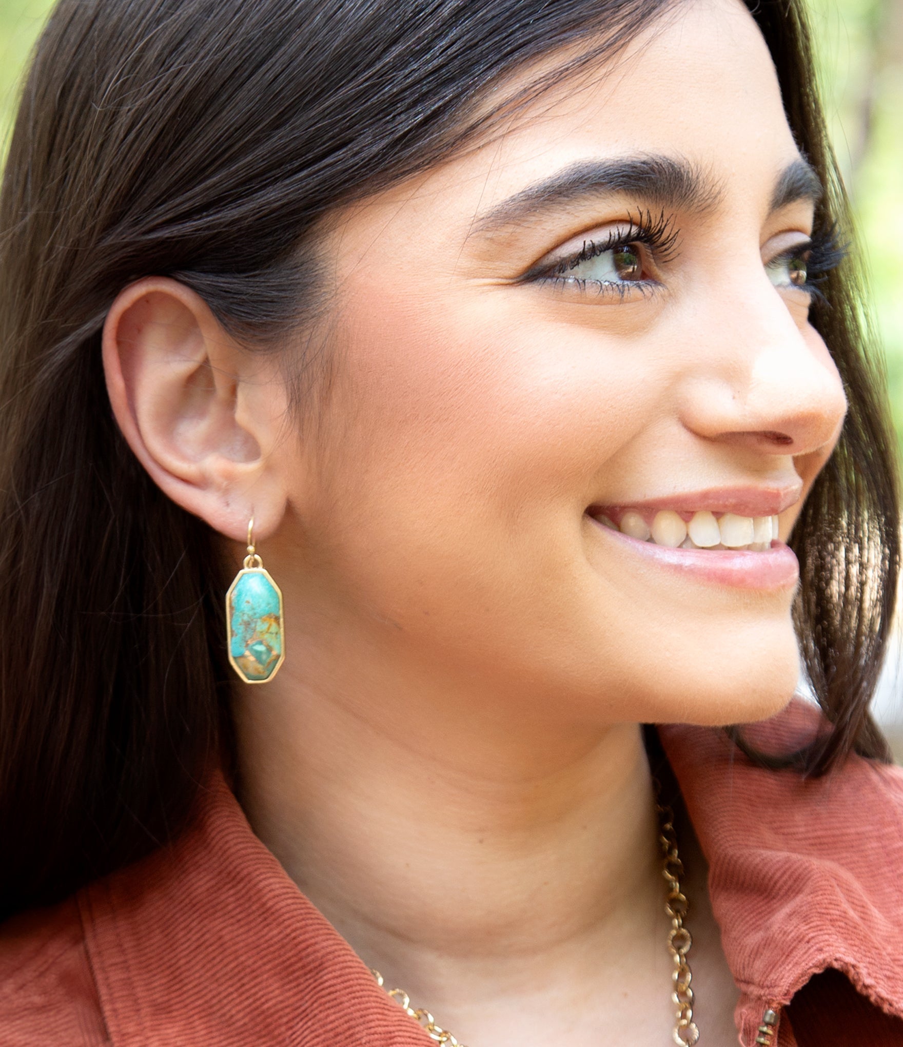 Close-up of a woman wearing turquoise earrings with a blurred natural background