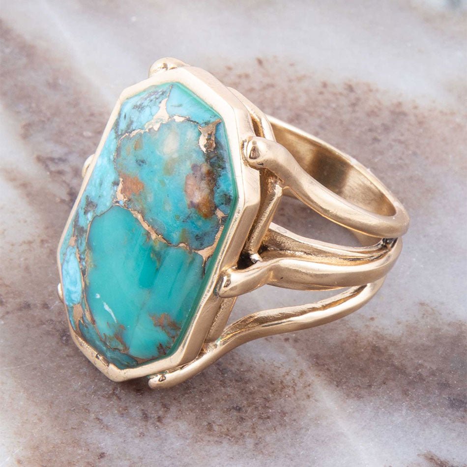 Gold ring with a large turquoise stone on a marble surface