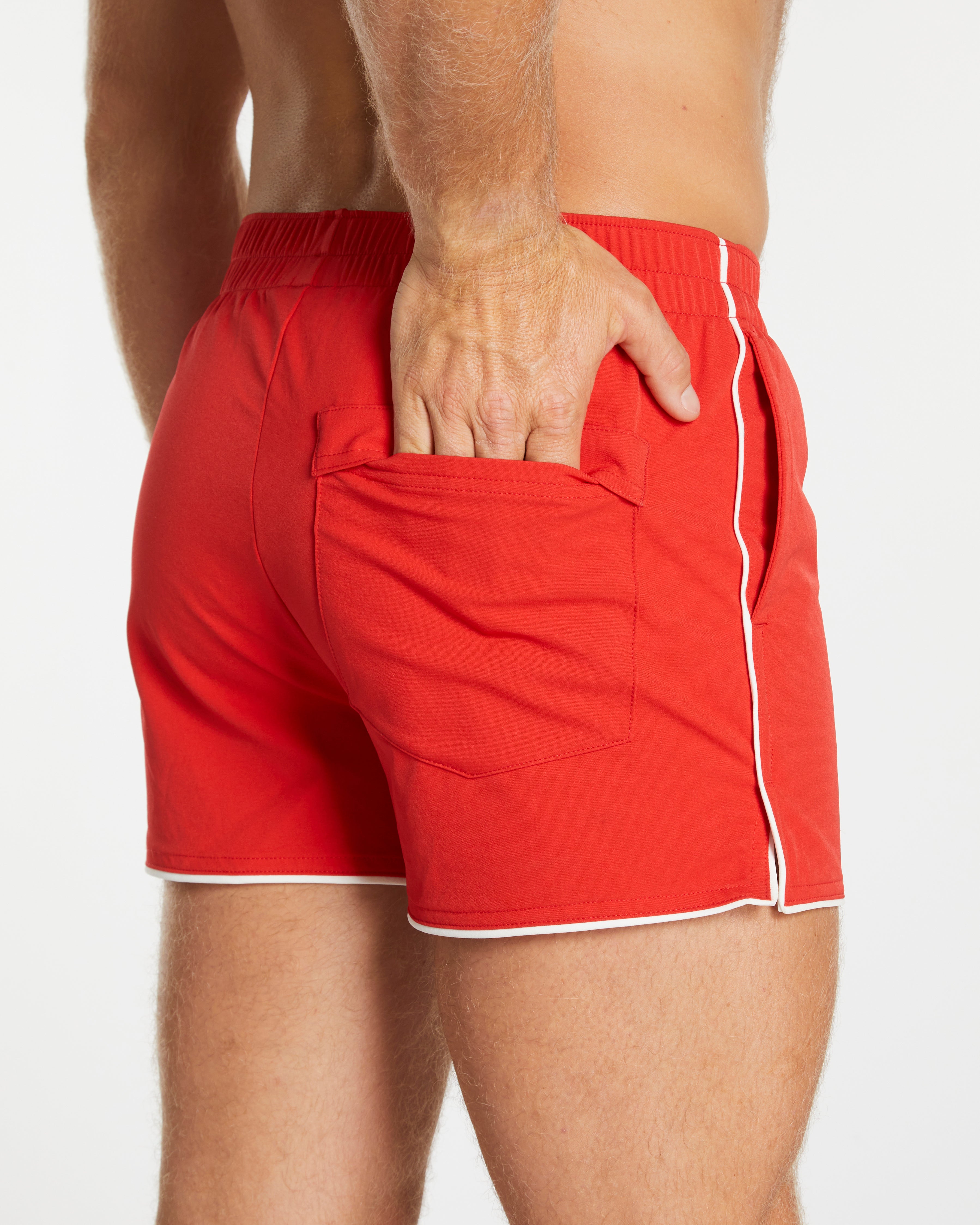 Red swim shorts with white trim worn by a person on a plain background