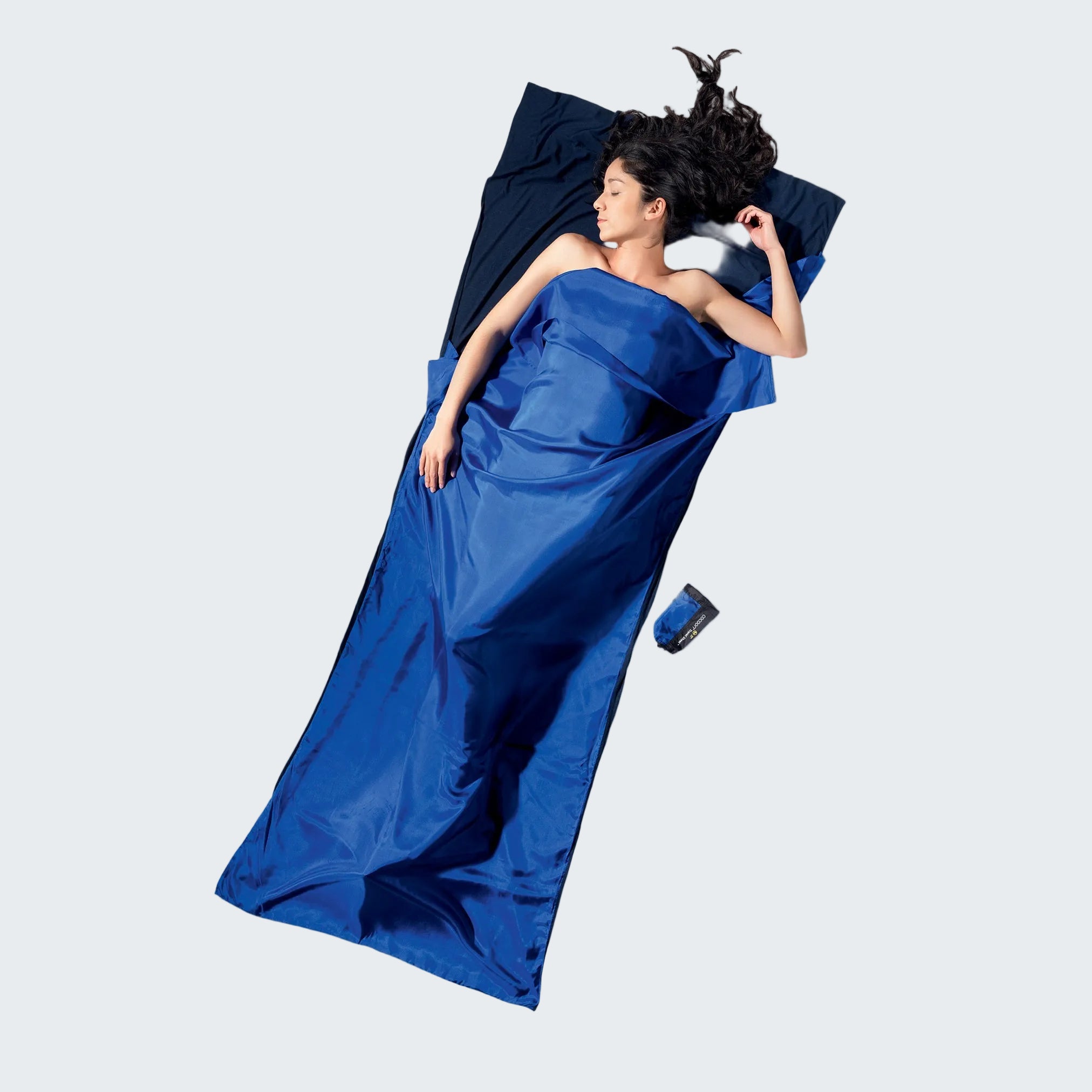 Woman lying on a gray surface wearing a blue dress and sleeping bag.