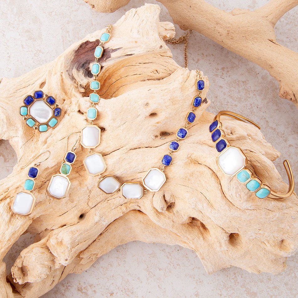 Pair of earrings with blue and turquoise stones on a piece of driftwood.