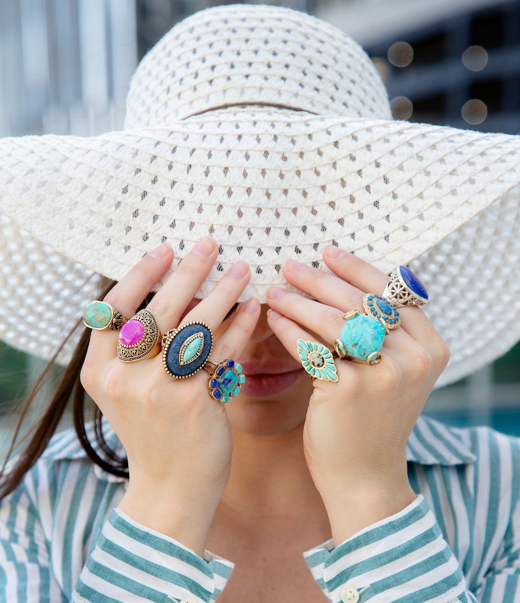 Person wearing a wide-brimmed hat and multiple colorful rings on their fingers.