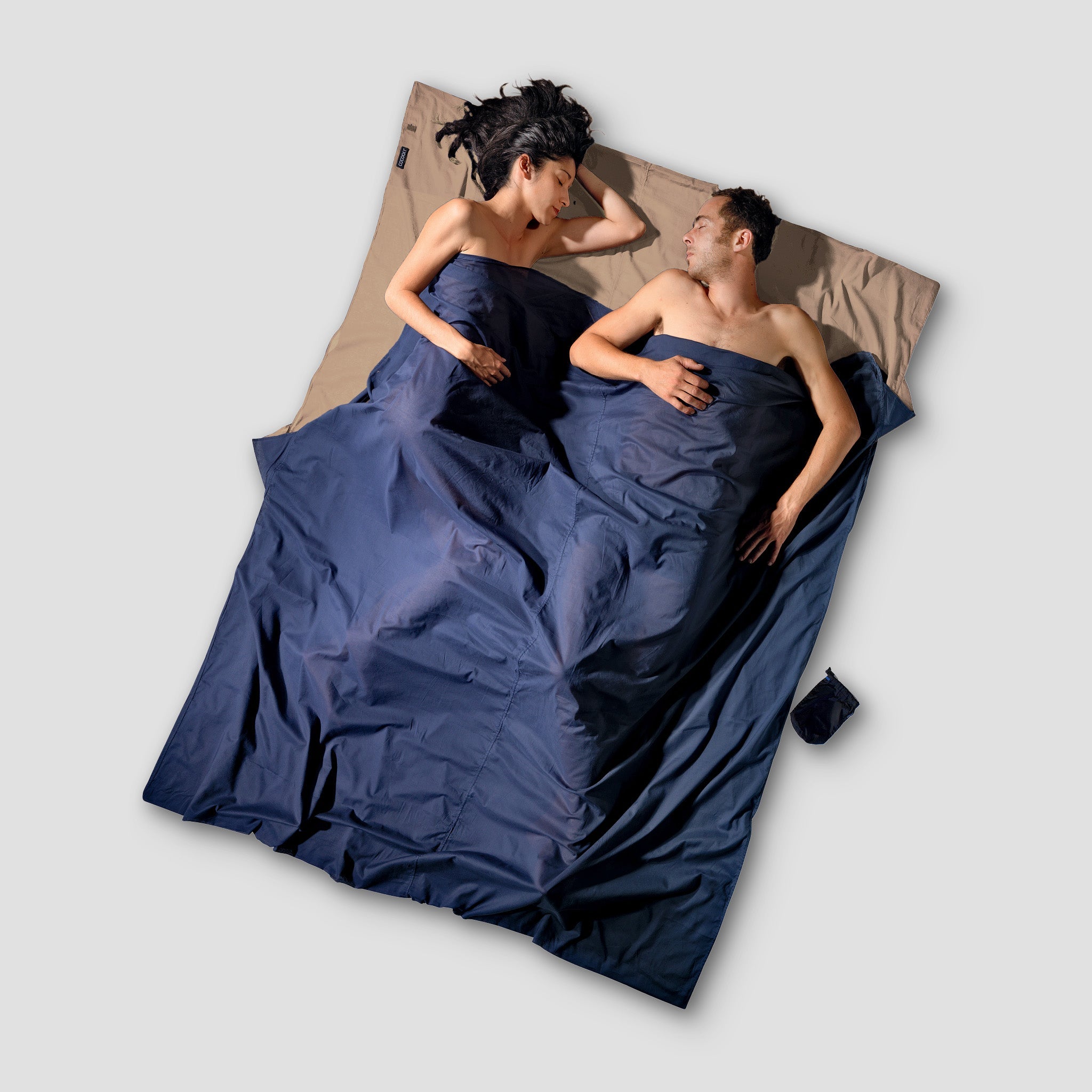 Two people lying on a large blue blanket against a neutral background