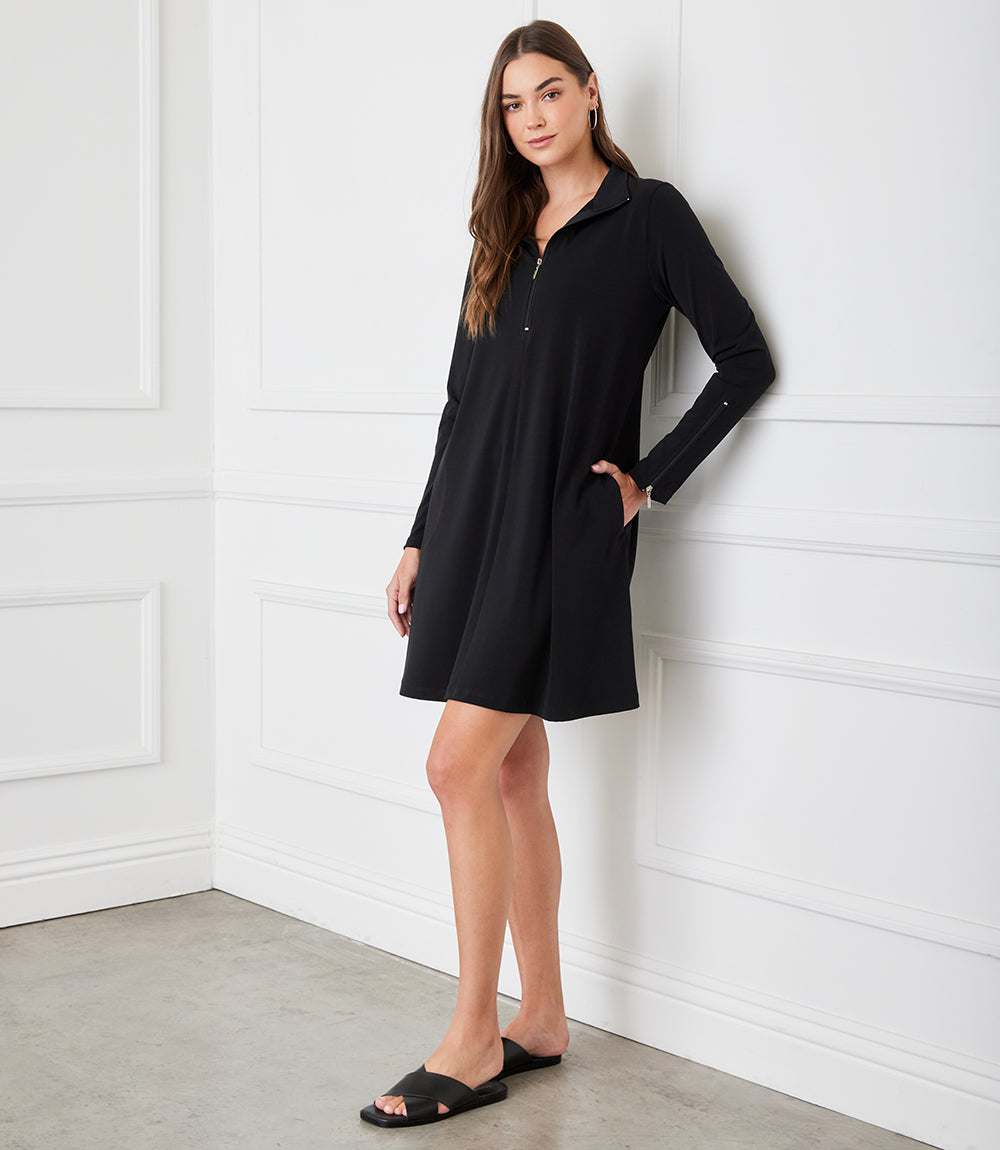 Woman wearing a black dress against a white paneled wall.