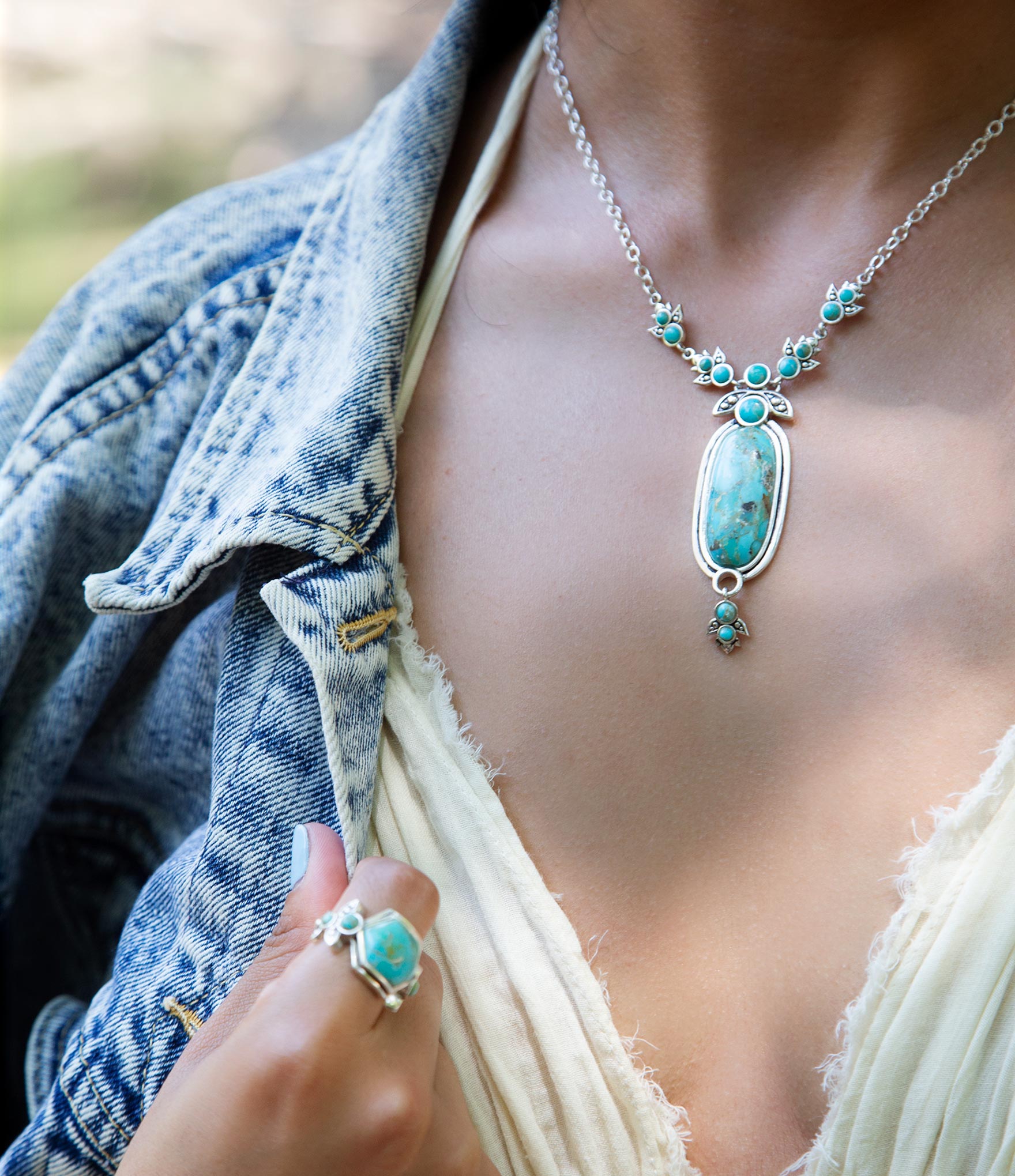Turquoise necklace and ring on a person wearing a denim jacket.