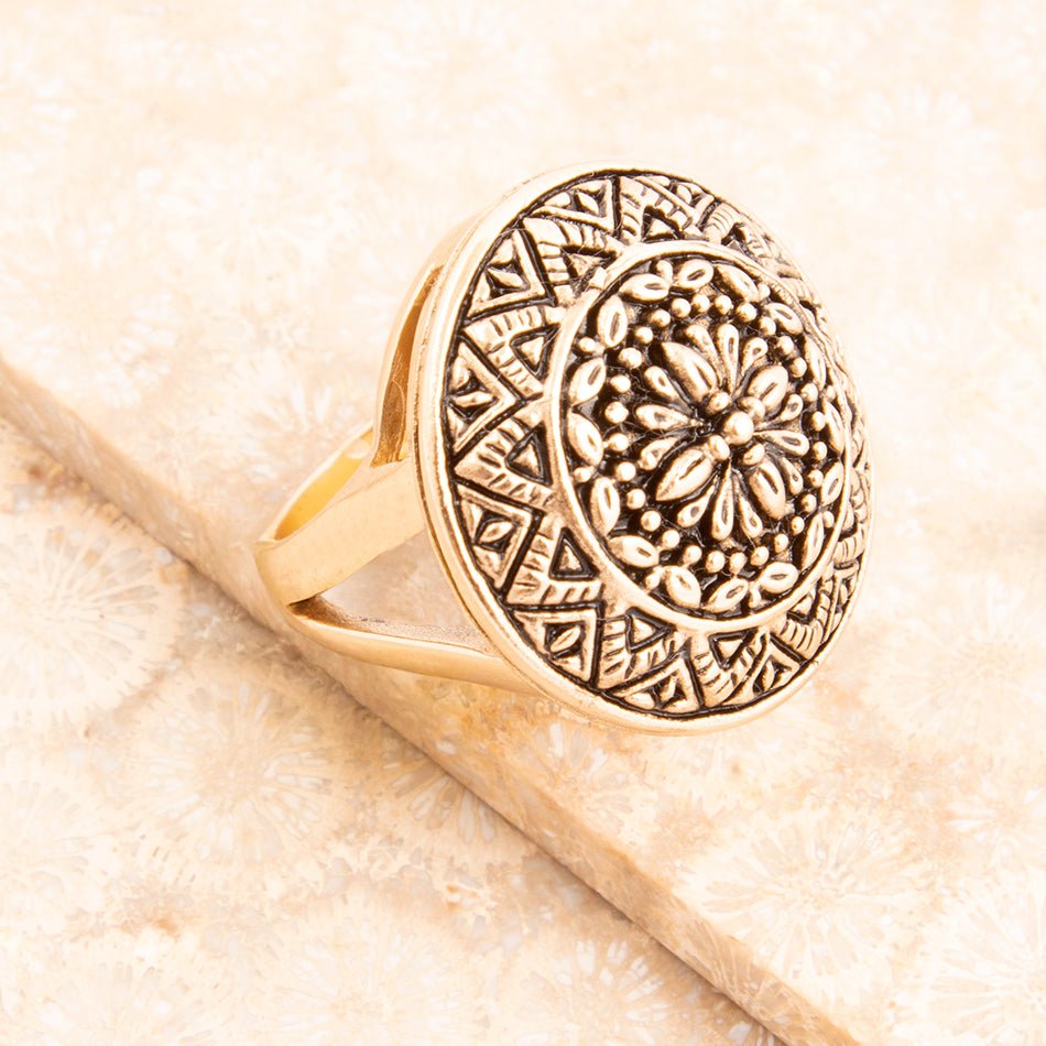 Gold ring with intricate design on a beige surface