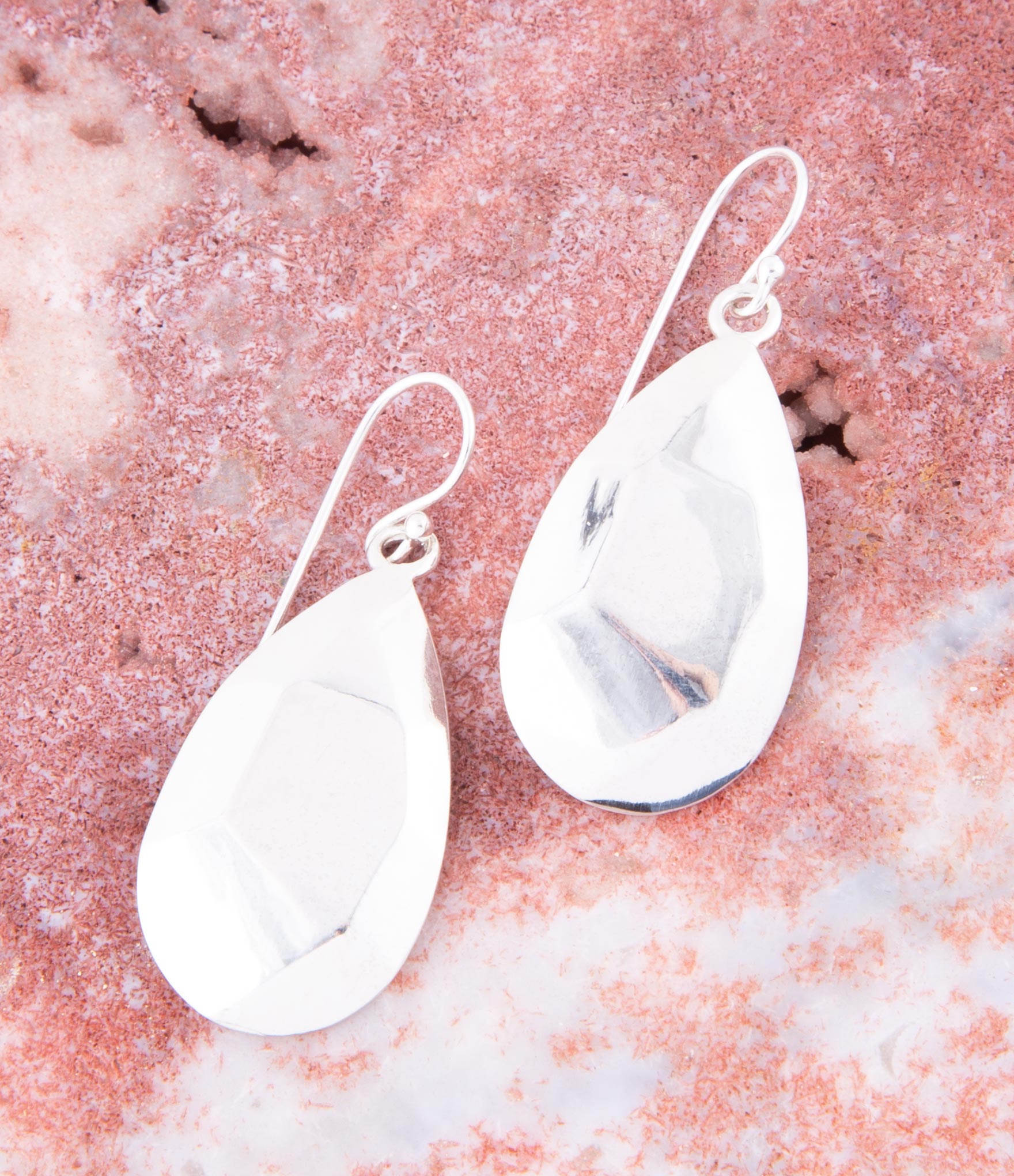 Teardrop-shaped earrings on a textured pink surface