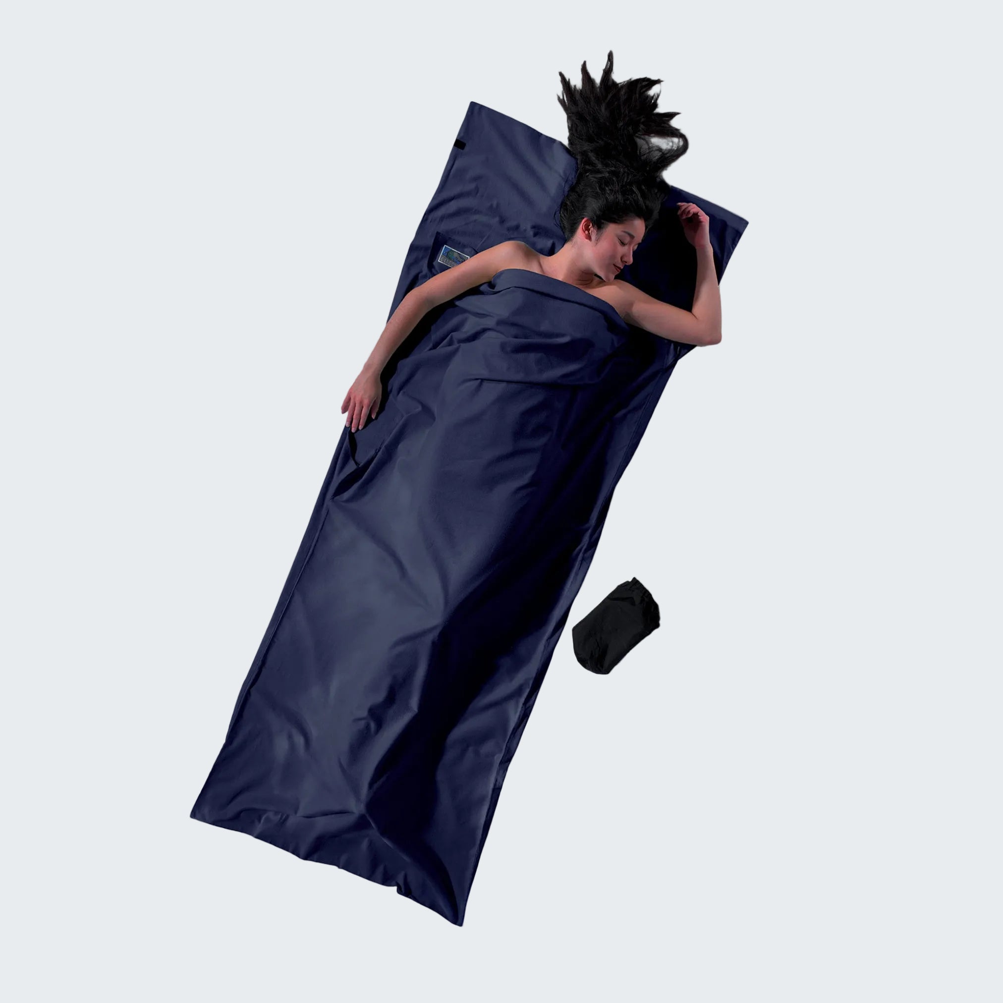 Person lying in a navy blue sleeping bag on a light gray background
