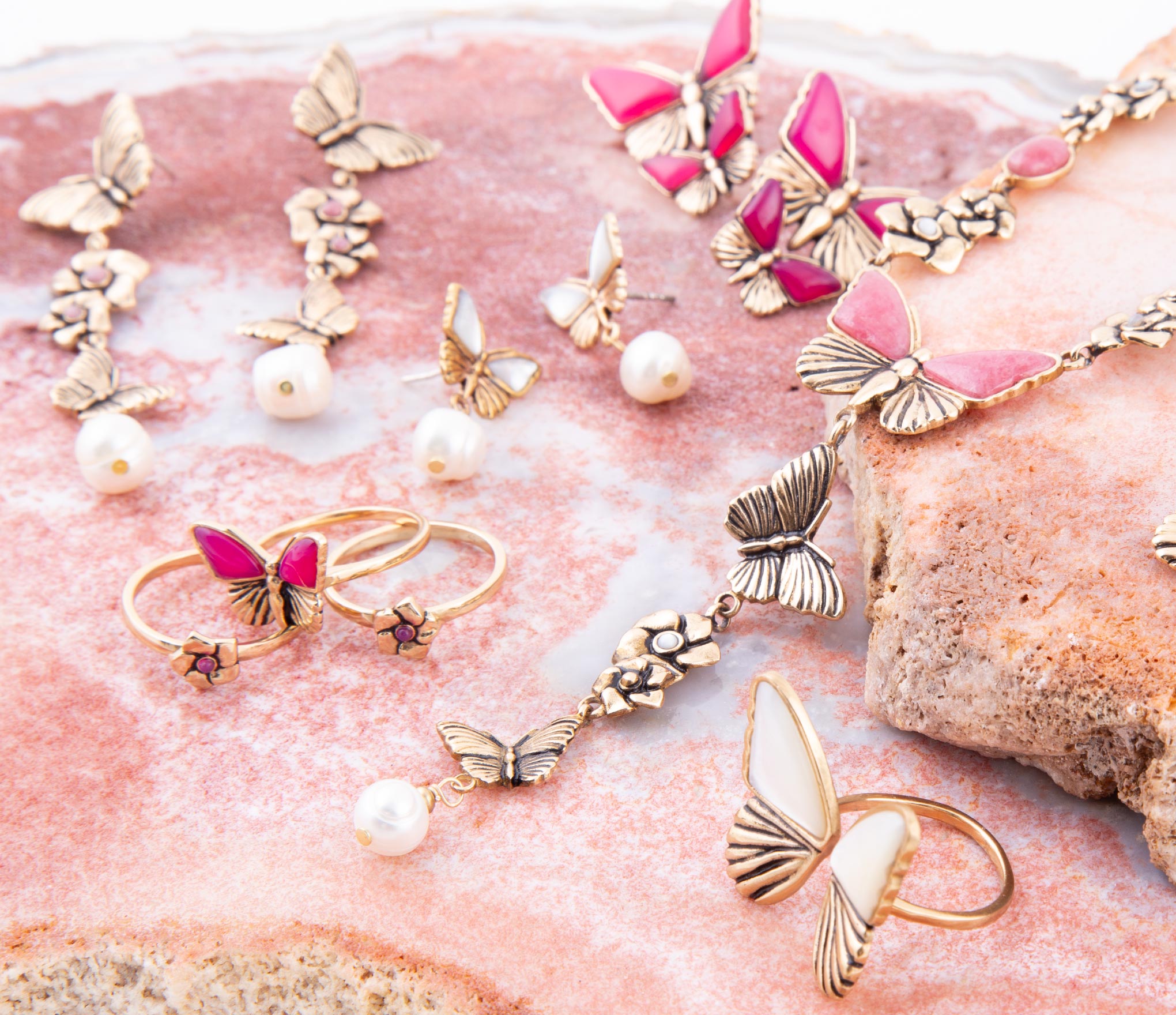Butterfly-themed jewelry including rings and pendants on a pink stone surface.