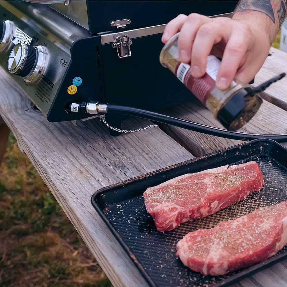Person seasoning raw steaks on a portable grill outdoors