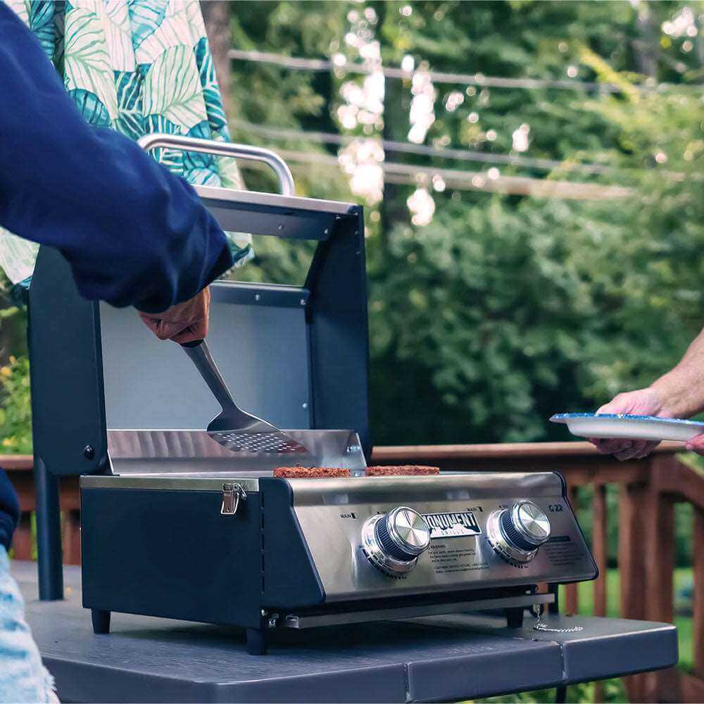 Person grilling outdoors using a portable barbecue grill on a deck.