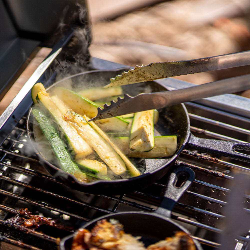 Zucchini being grilled in a cast iron skillet on a barbecue grill.