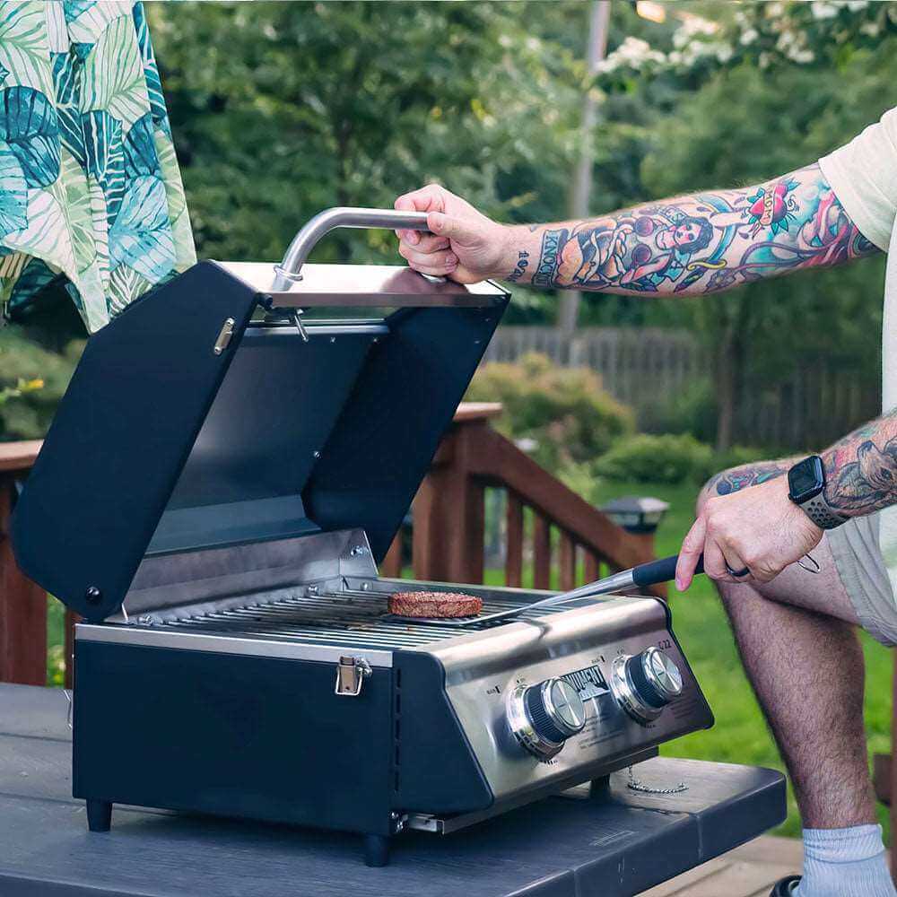 Person grilling a burger on a portable grill outdoors
