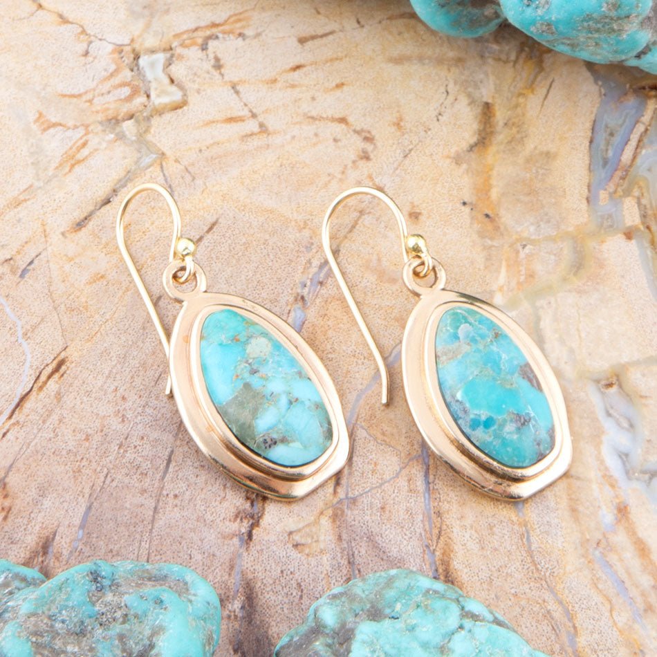 Gold earrings with turquoise stones on a stone surface