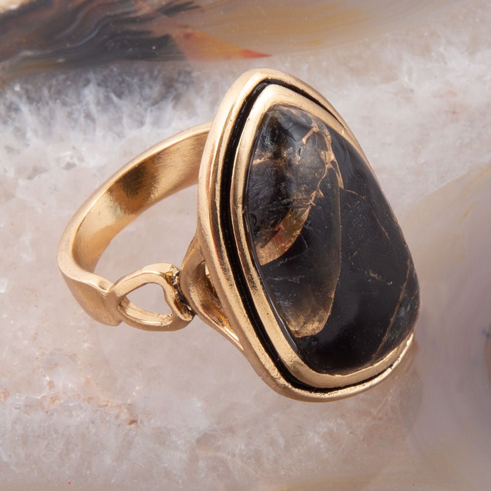 Gold ring with a large black stone on a marble surface