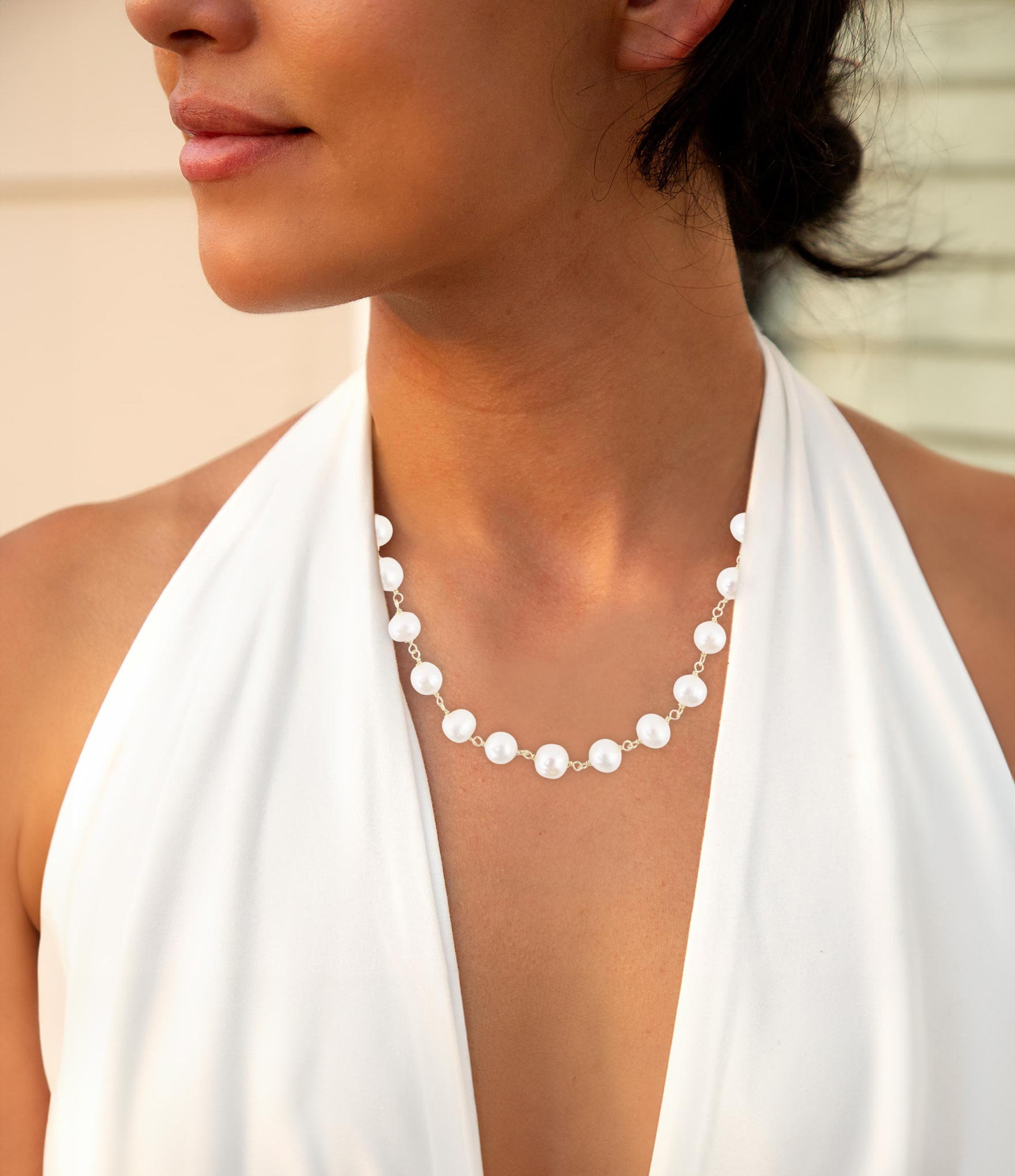Woman wearing a pearl necklace with a white top against a neutral background