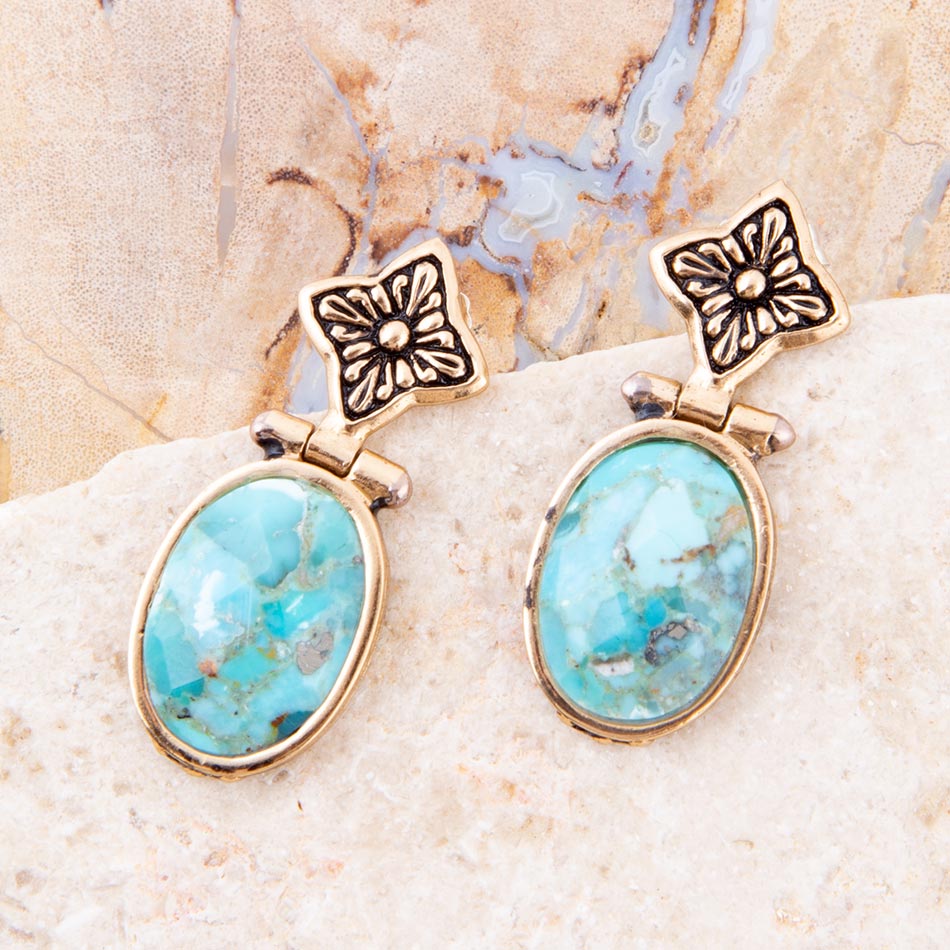 Gold earrings with turquoise stones on a textured beige surface