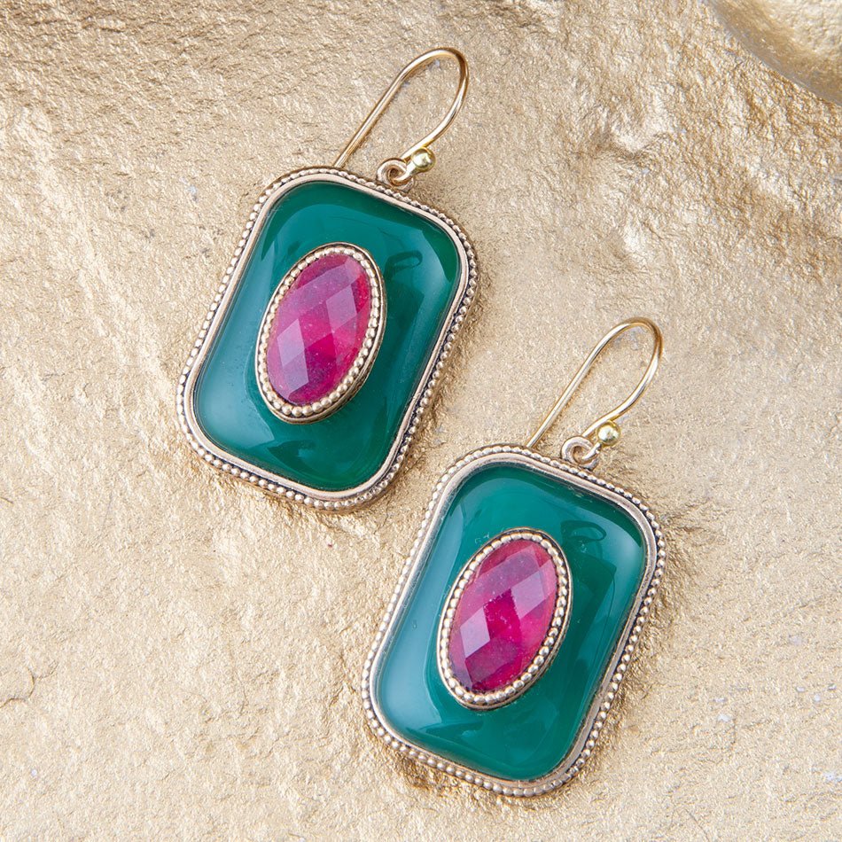 Pair of earrings with green and pink stones on a textured beige background