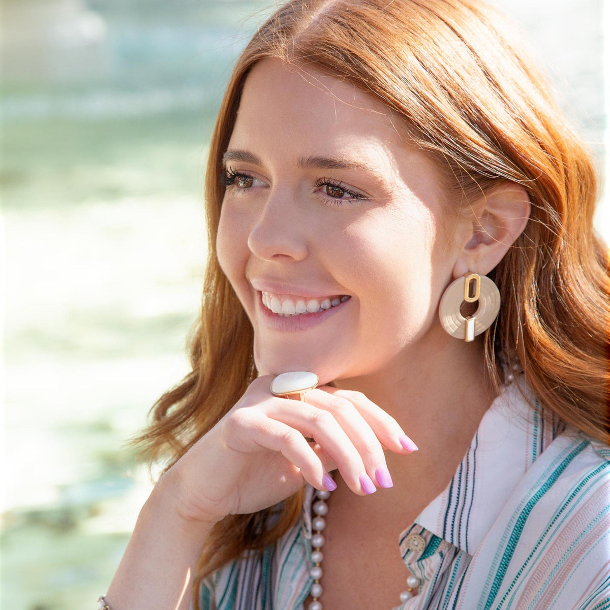 Woman wearing gold earrings and a striped shirt with a blurred natural background