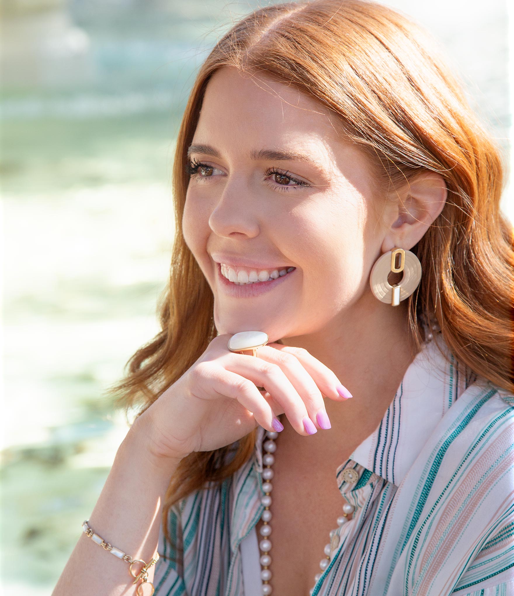 Woman wearing gold earrings and a striped shirt with a blurred natural background