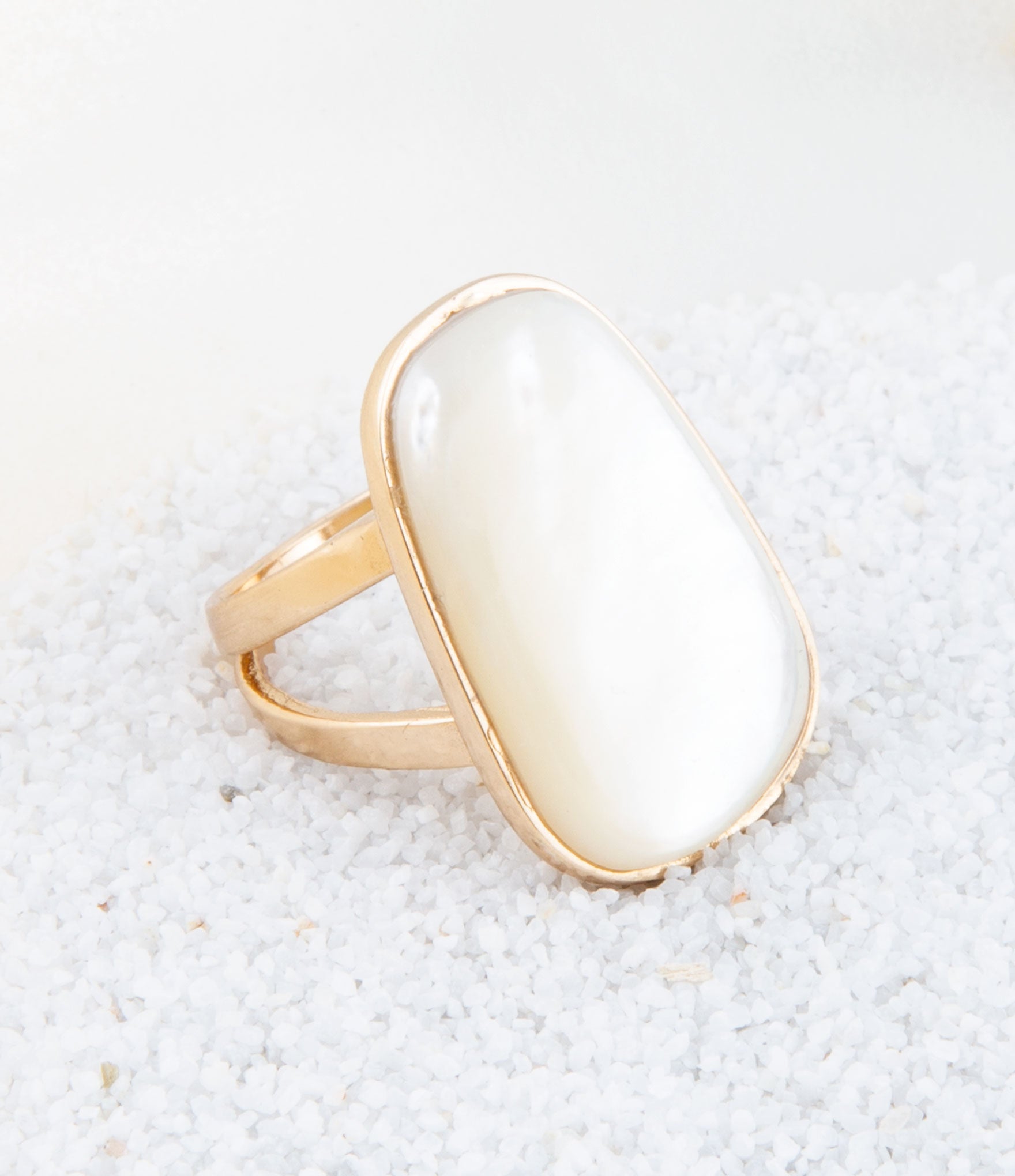 Gold ring with a large white stone on a textured beige surface