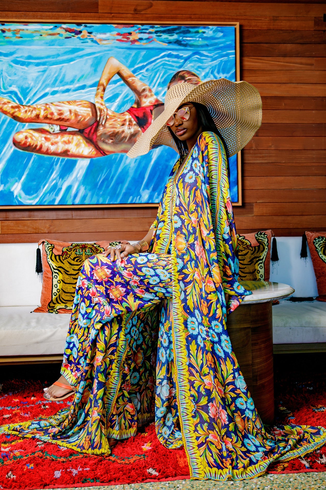 Woman in a colorful outfit sitting on a couch with a vibrant painting in the background
