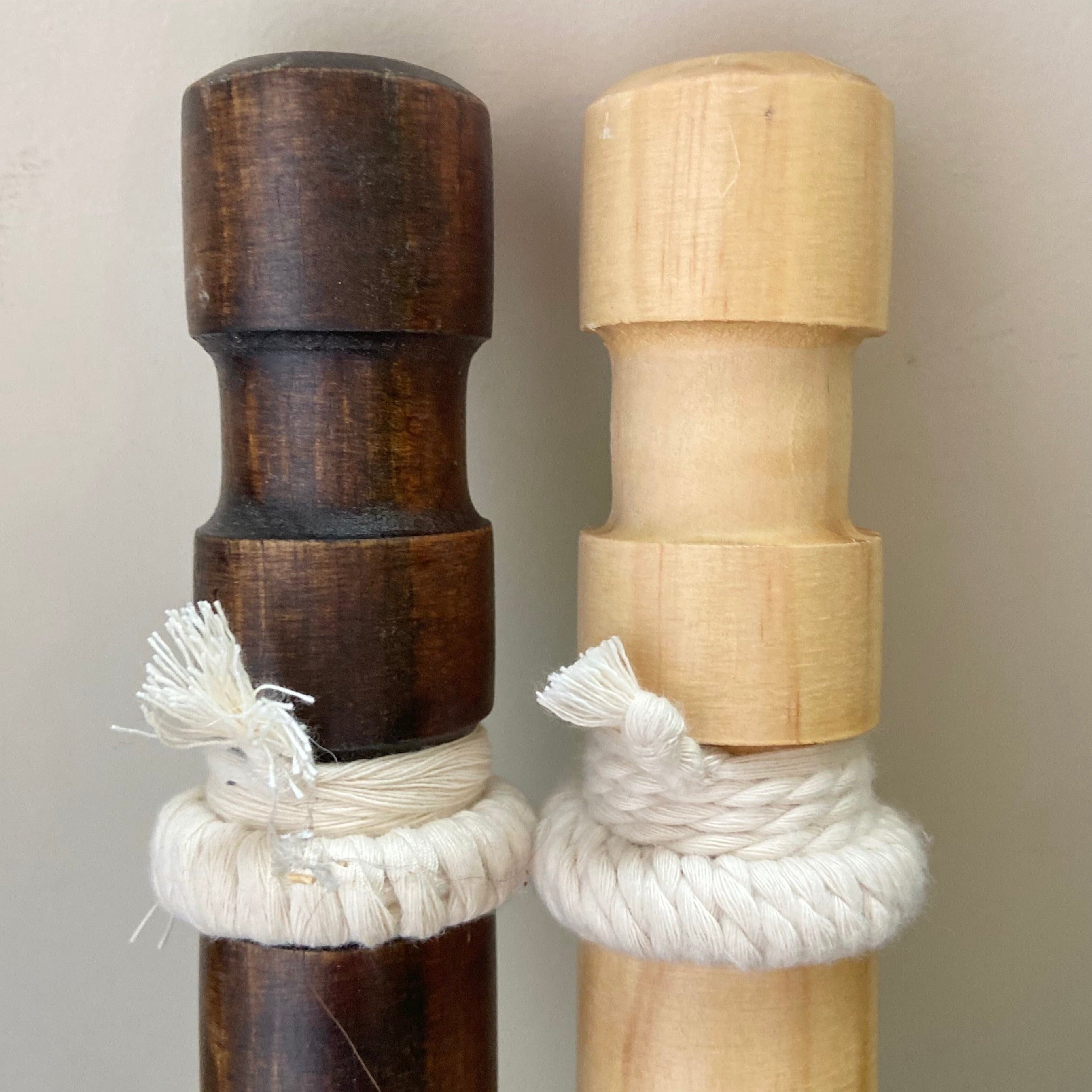 Two wooden sticks with rope wrapping, one dark brown and one light brown, on a neutral background.