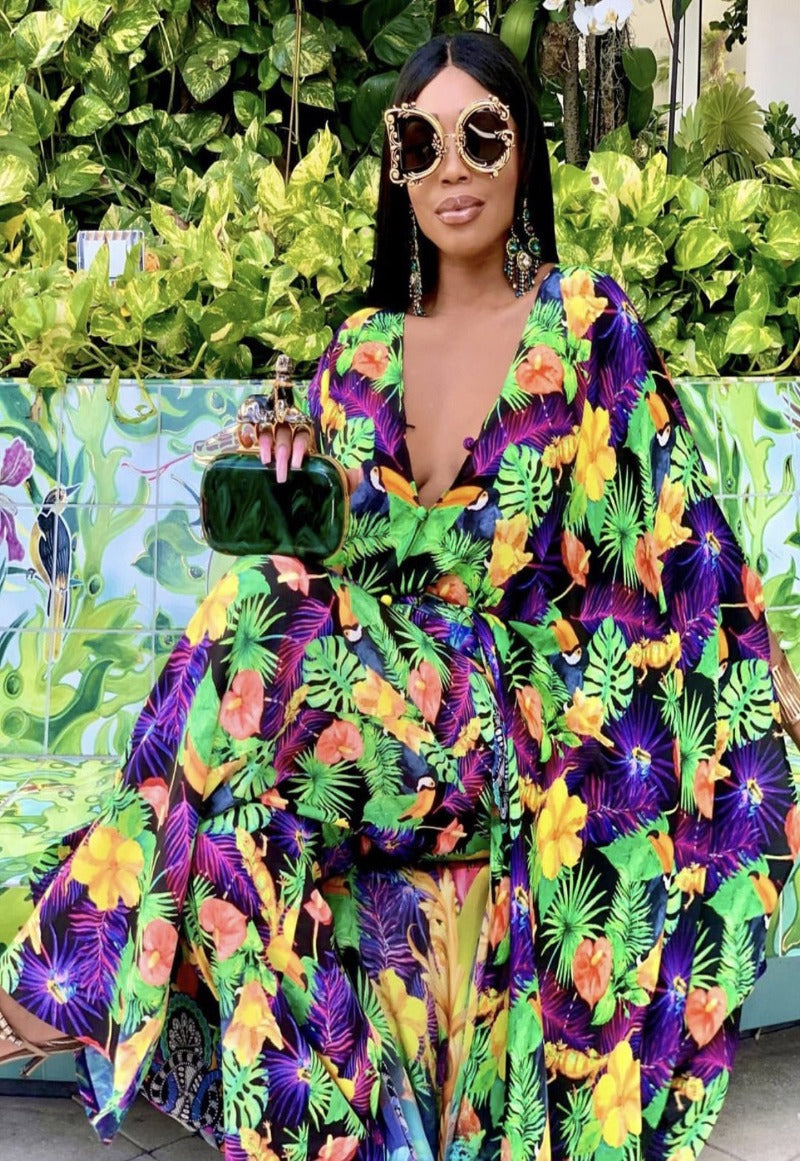 Woman in a colorful floral dress standing in front of green foliage