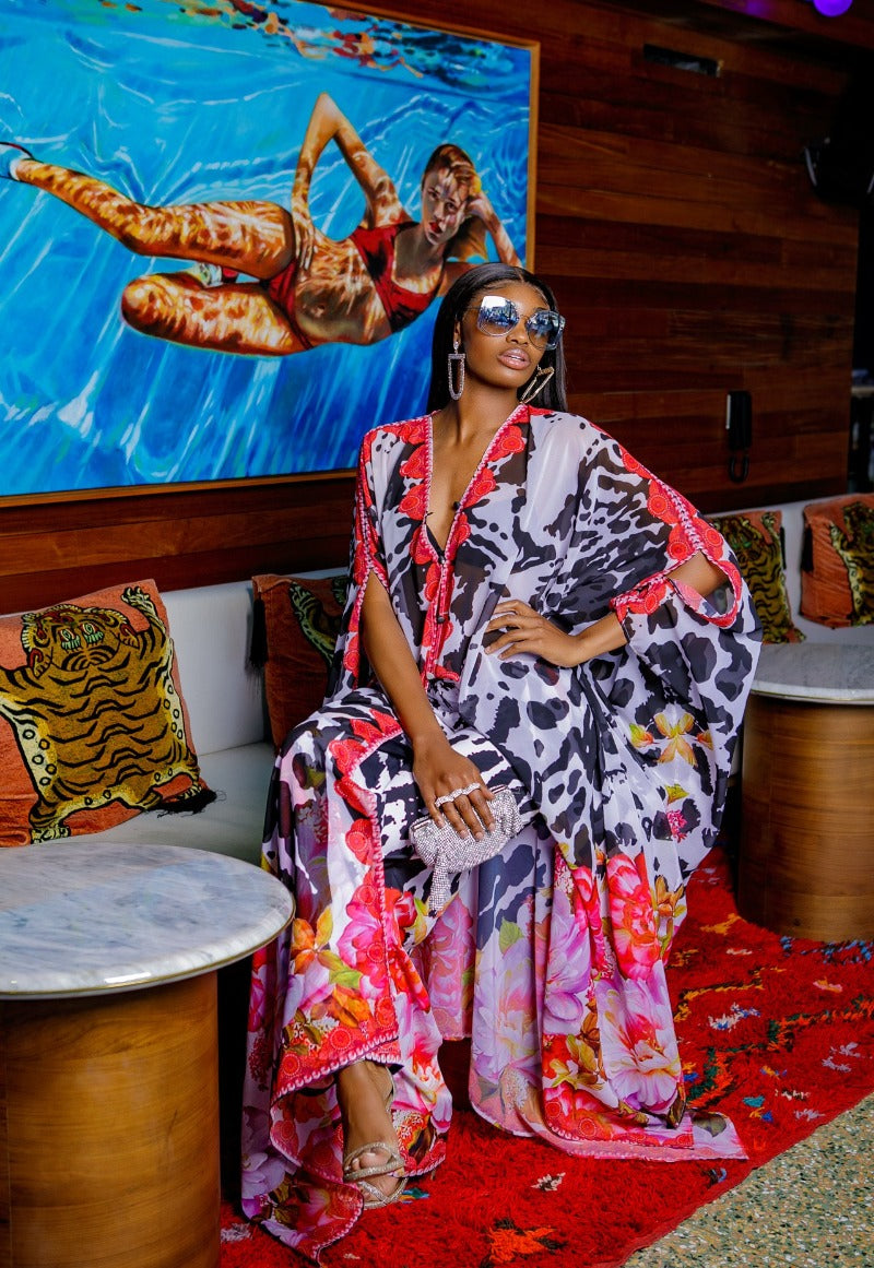 Woman in a colorful dress sitting on a couch with a TV in the background showing people swimming.