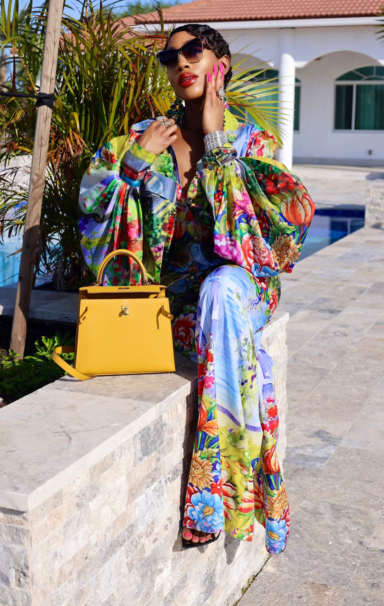 Woman in a colorful outfit with a yellow handbag by a poolside.