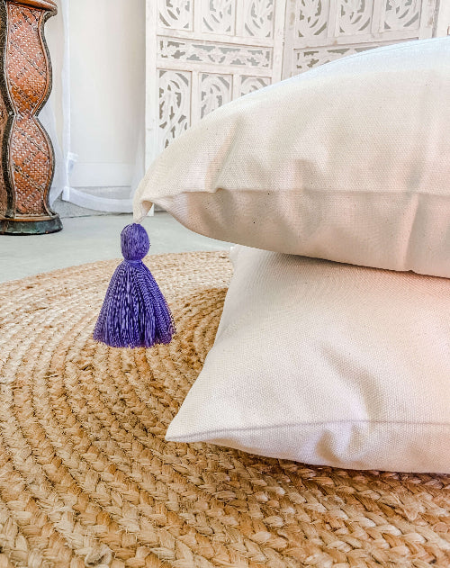 Beige pillows with a purple tassel on a woven mat