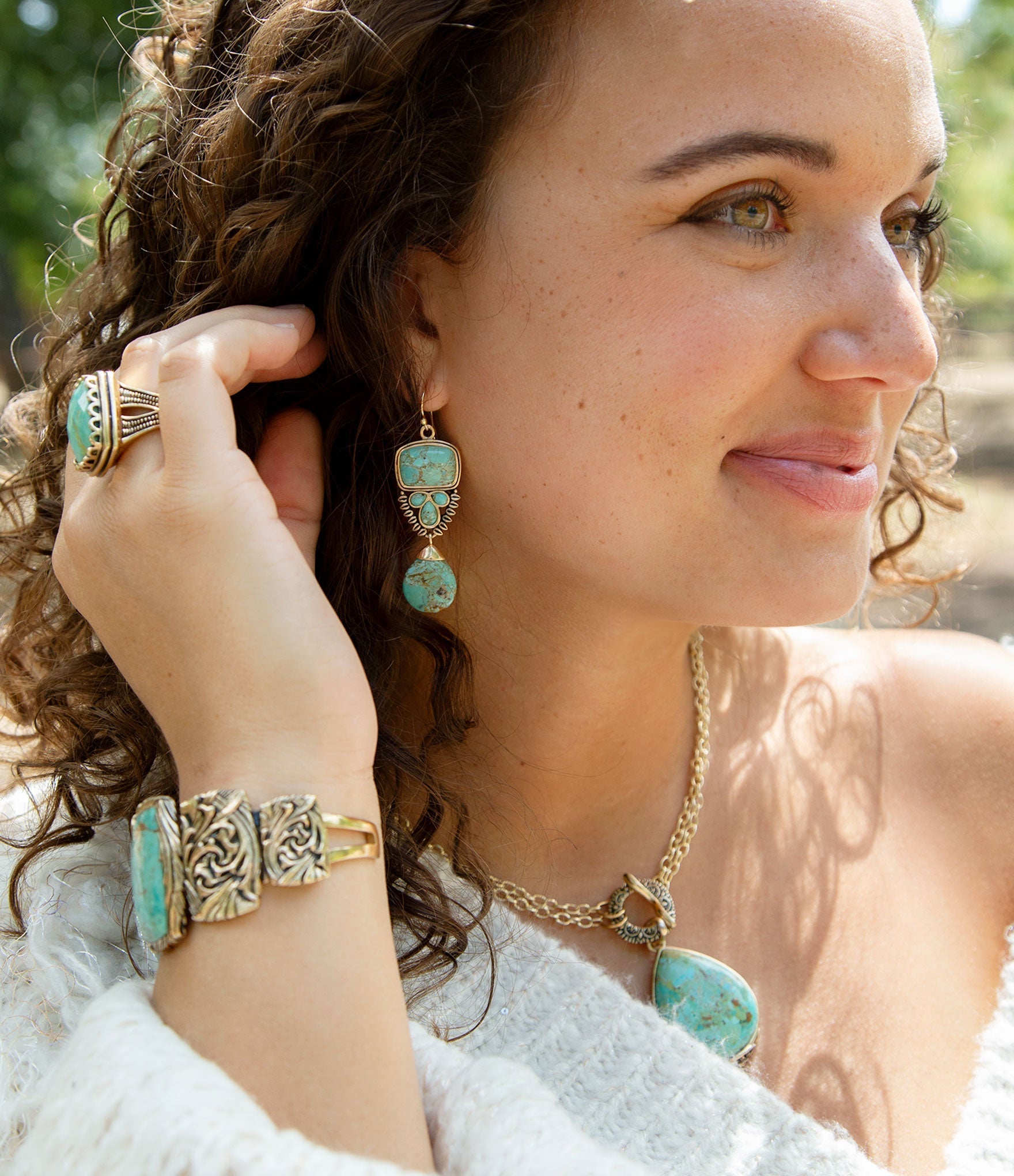 Woman wearing turquoise jewelry including earrings, ring, and bracelet outdoors.