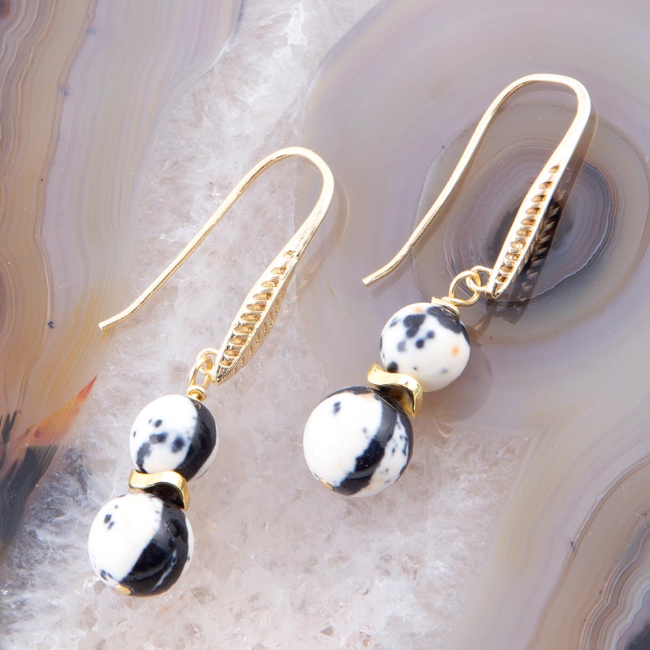 Gold earrings with black and white speckled beads on a textured surface