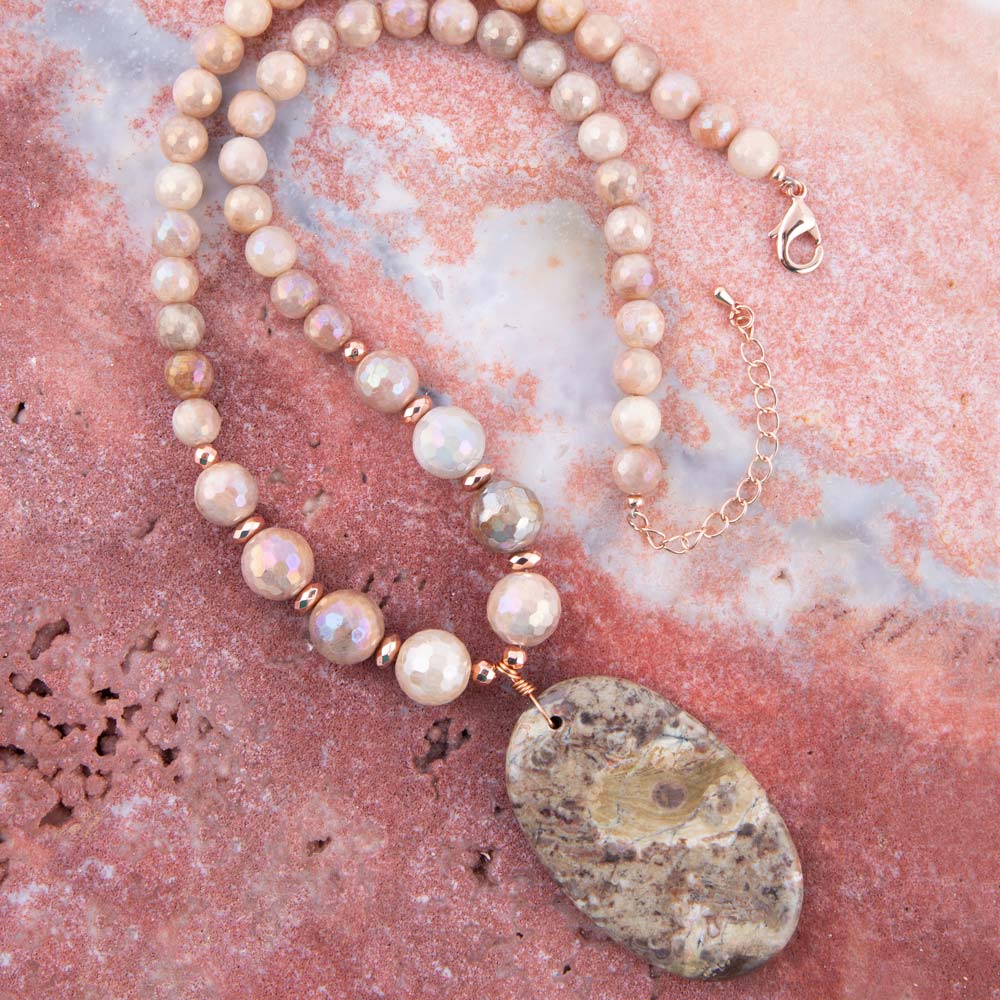 Pearl necklace with a large stone pendant on a pink marbled surface