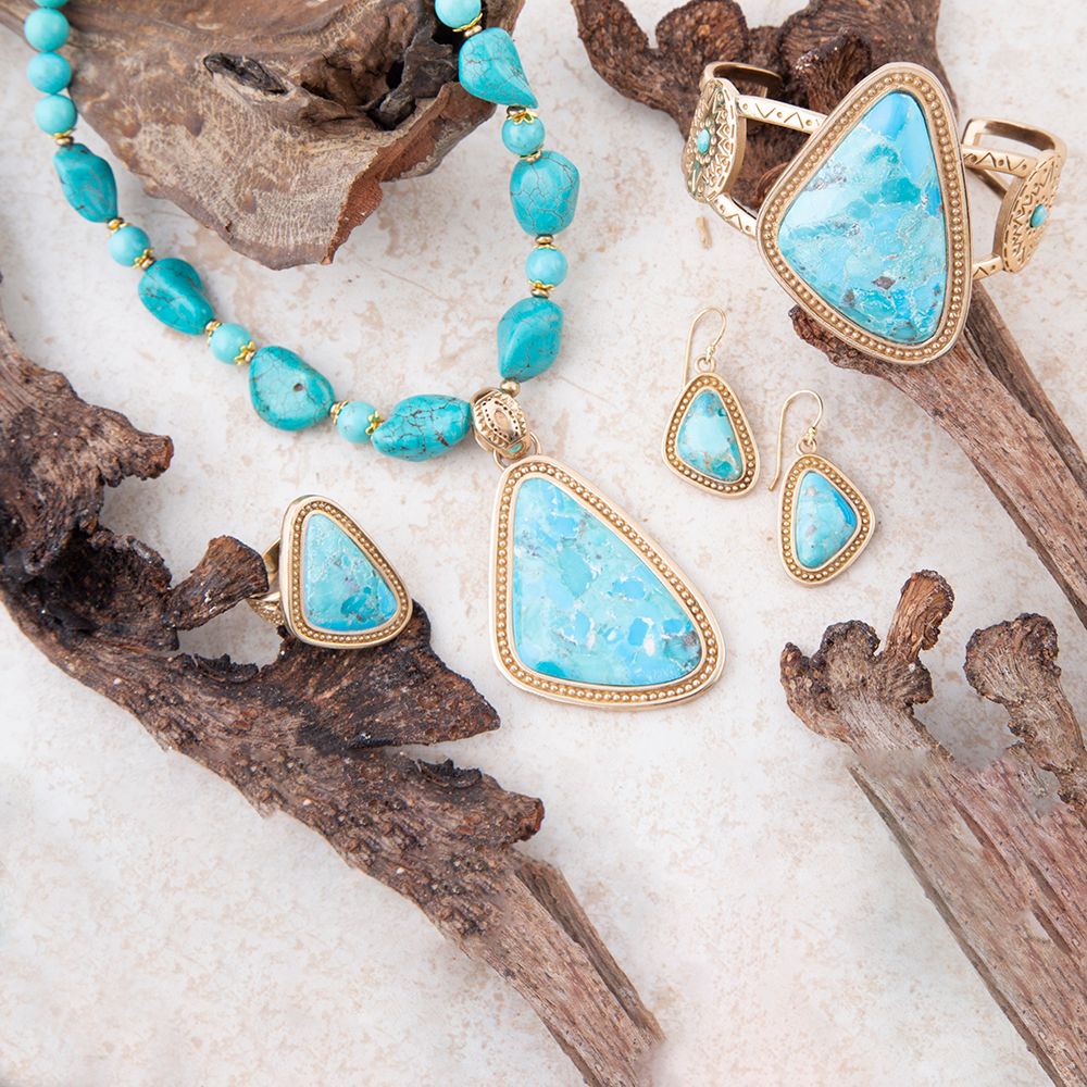 Turquoise jewelry set with necklace, ring, and earrings on a sandy background