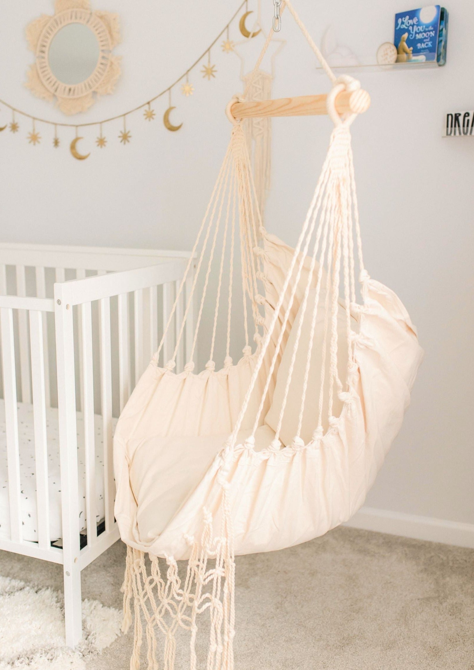 White hammock chair in a nursery with a crib and decorative items on the wall.