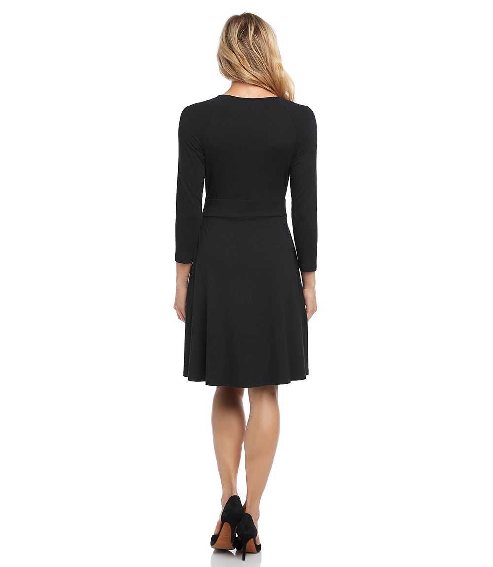 A woman viewed from the back wearing a black long-sleeve knee-length dress with a flared skirt, paired with black high heels, against a plain white background.