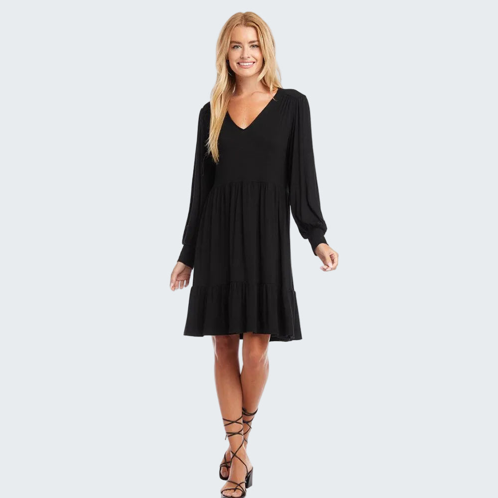 A woman modeling a long-sleeve navy blue V-neck dress with a tiered skirt, paired with black lace-up heeled sandals, against a plain white background.