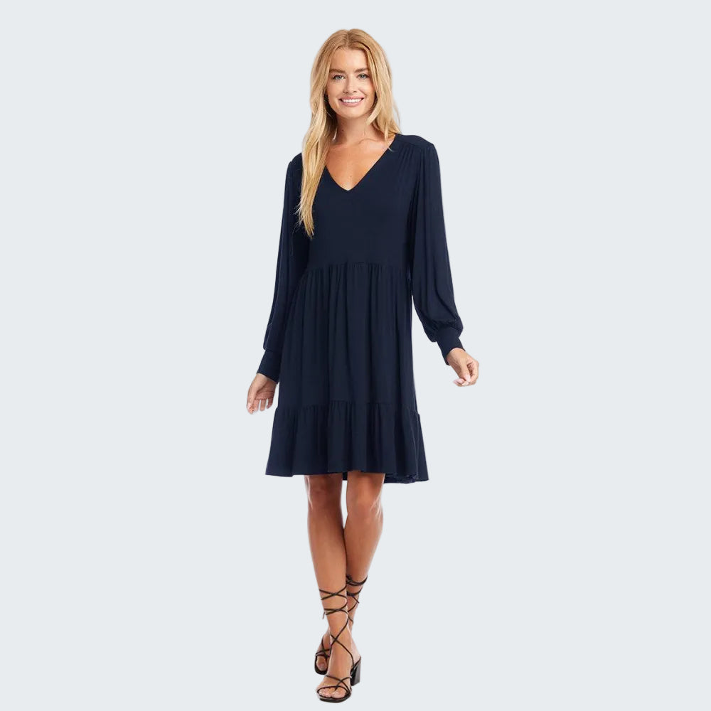 A woman modeling a long-sleeve navy blue V-neck dress with a tiered skirt, paired with black lace-up heeled sandals, against a plain white background.
