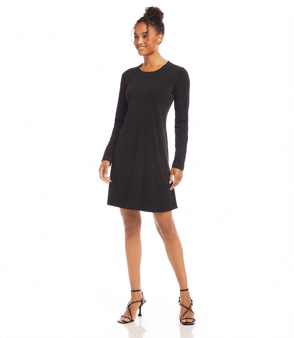 A woman modeling a black long-sleeve shift dress with a crew neckline, paired with black strappy high-heeled sandals, against a plain white studio background.
