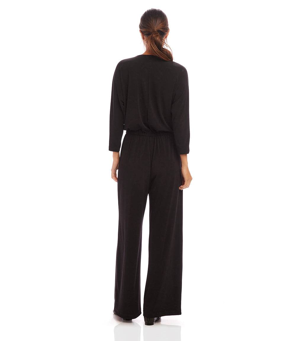 A woman viewed from the back wearing a black three-piece jumpsuit with long sleeves, a crew neck, and wide-leg pants, set against a plain white background.