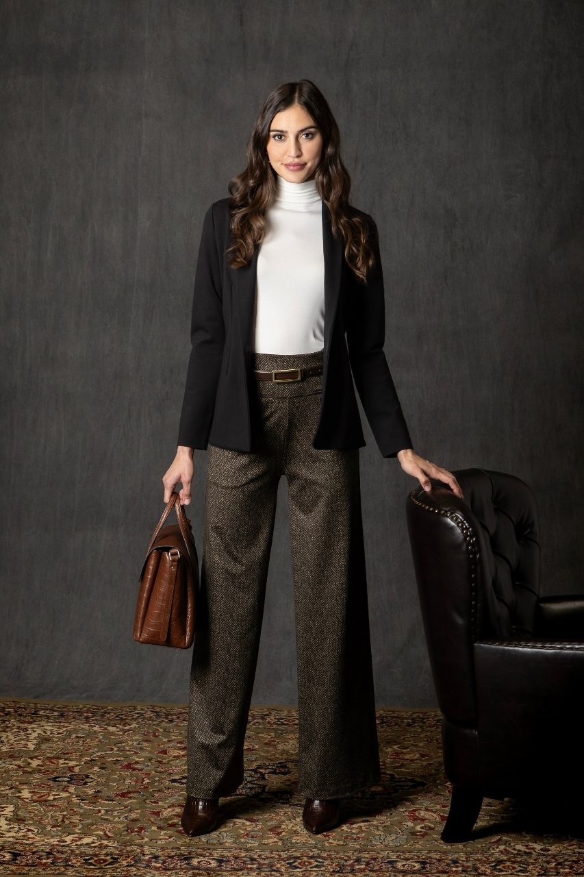 Woman in formal attire holding a brown leather bag against a dark background
